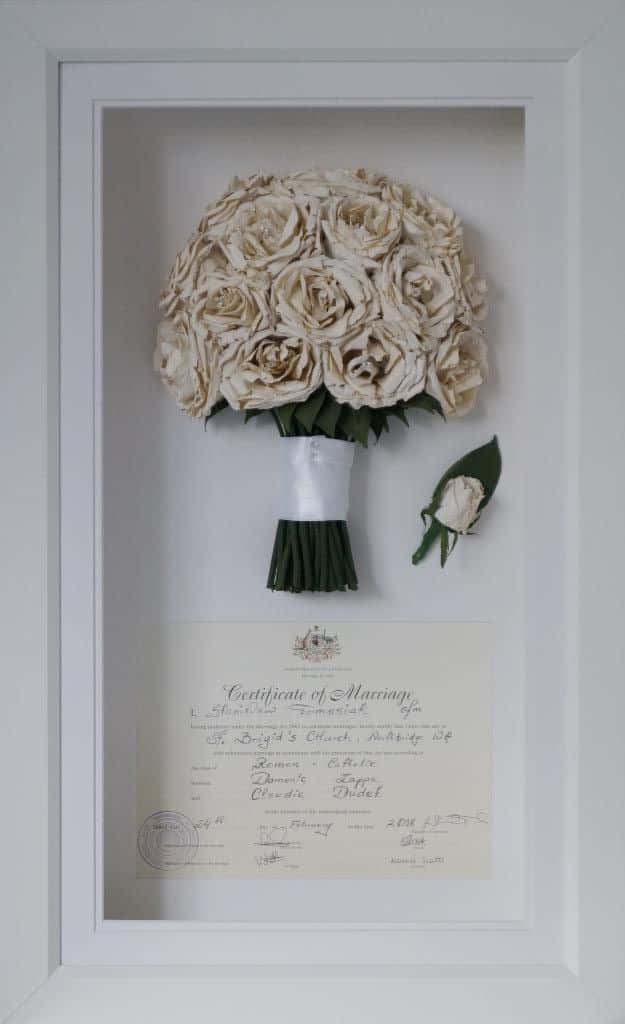 Roses Wedding 桌布 壁紙 — 保存的奶油色玫瑰花束和胸花展示在白色相框中，置於復古結婚證書上方。