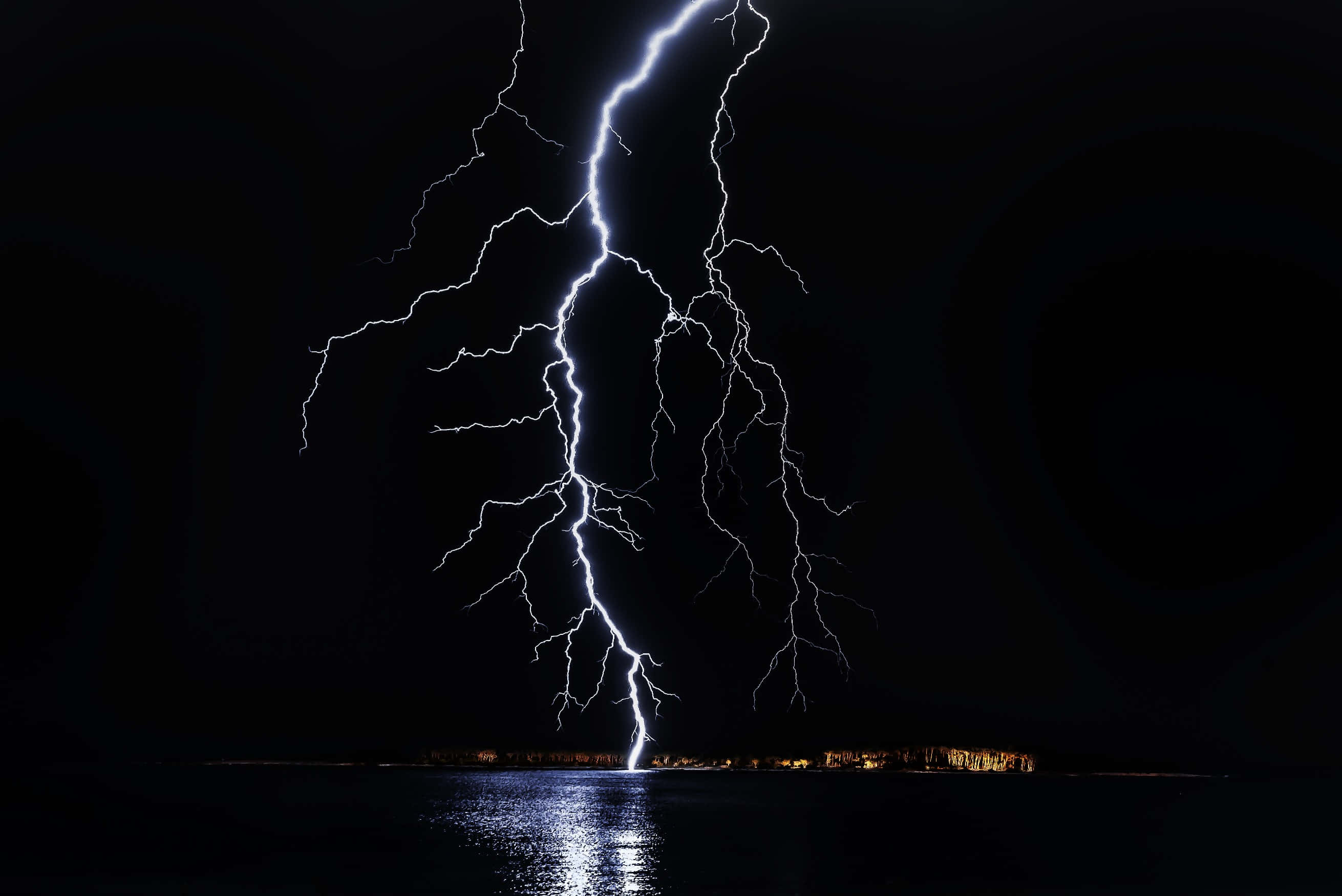 保持冷靜，保持酷炫 壁紙 — 一道巨大的閃電在夜間劃過黑暗的湖泊，照亮了水面和遠處的岸邊燈光。