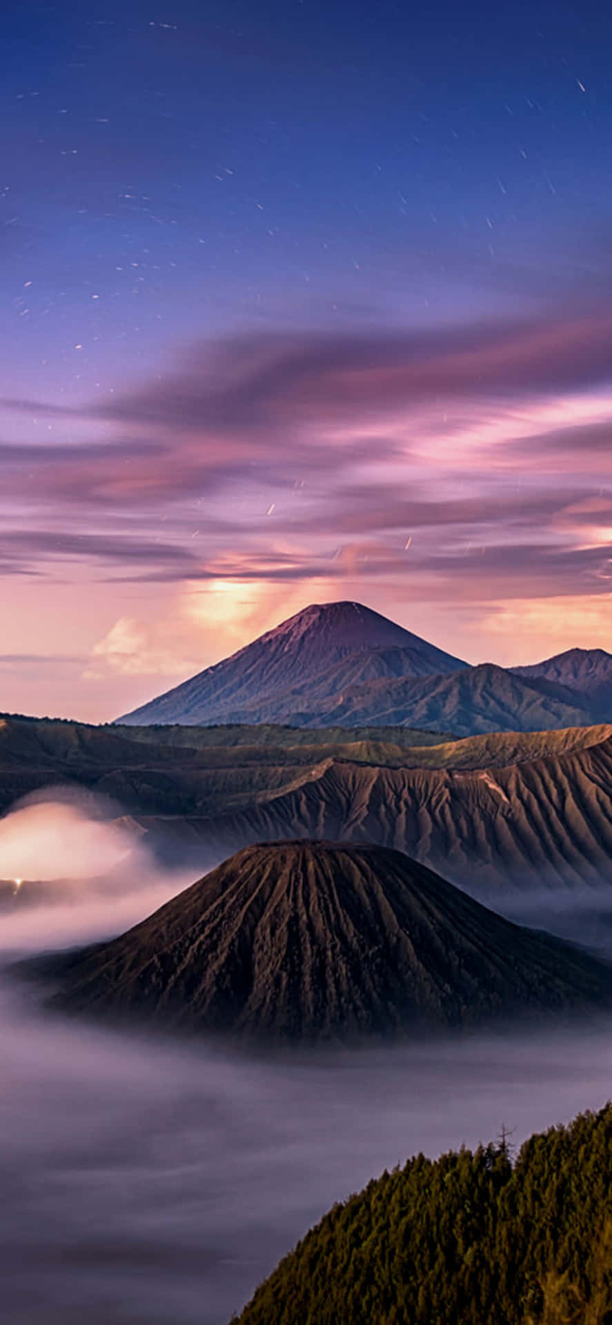火山峰在星空暮色天空下聳立於霧雲之上。