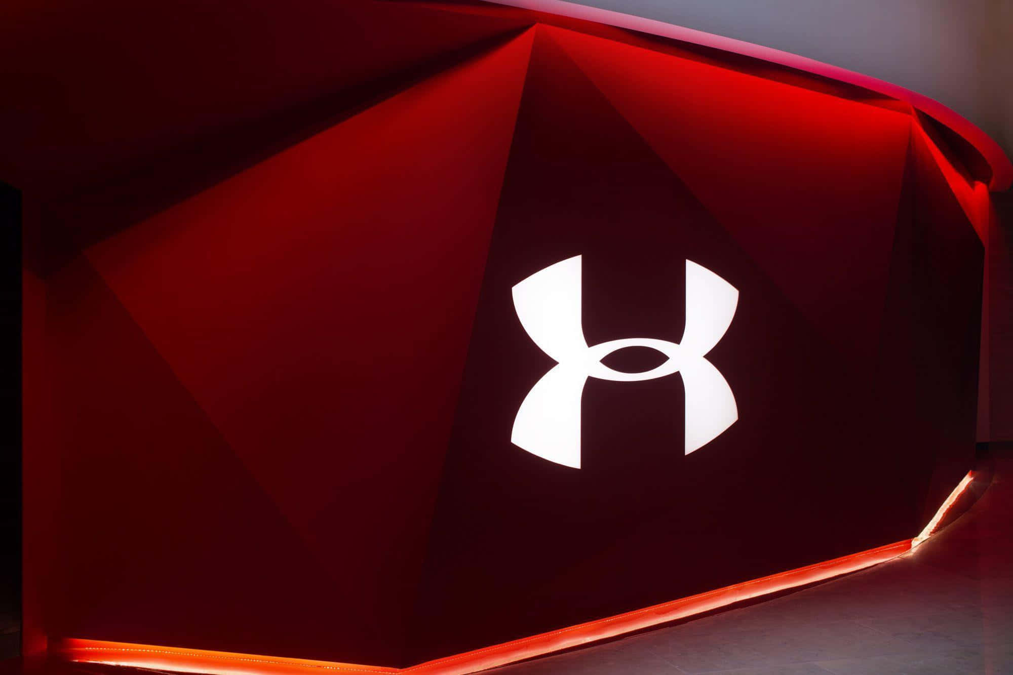 保持活力，持續前進，Under Armour伴你同行。 壁紙 — 發光的白色 Under Armour 標誌置中於幾何紅色牆壁上，帶有環境照明點綴。