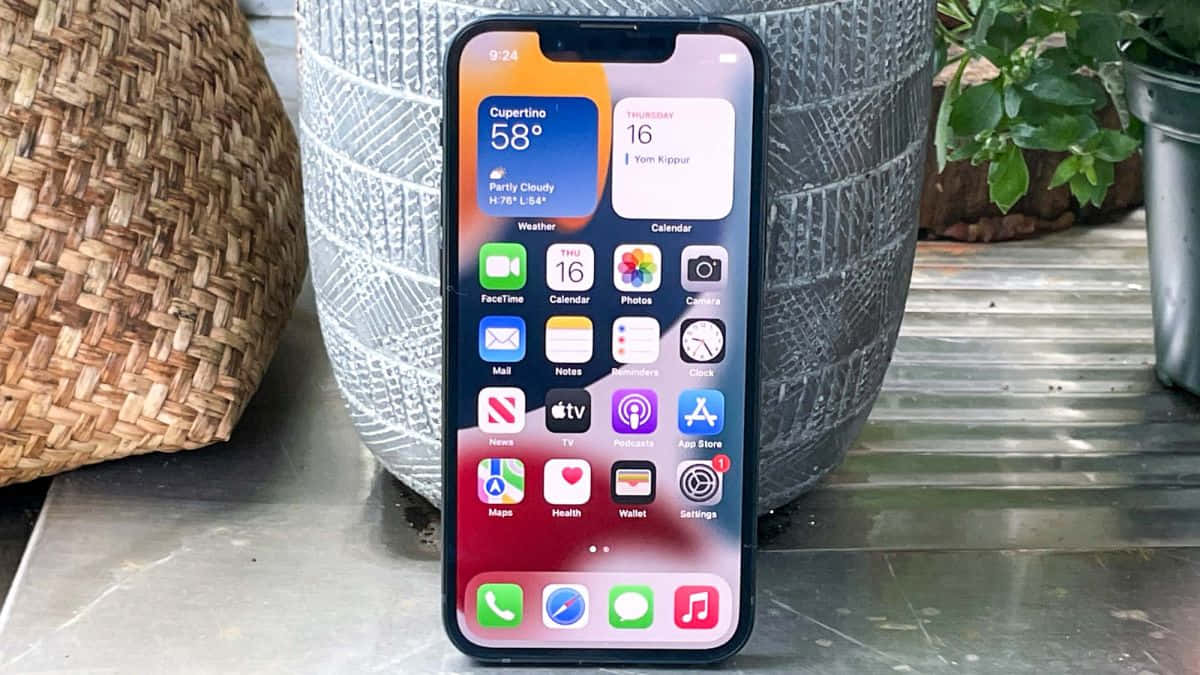 iPhone在金屬桌上顯示帶有應用程式和天氣詳情的主屏幕，靠近花盆。
