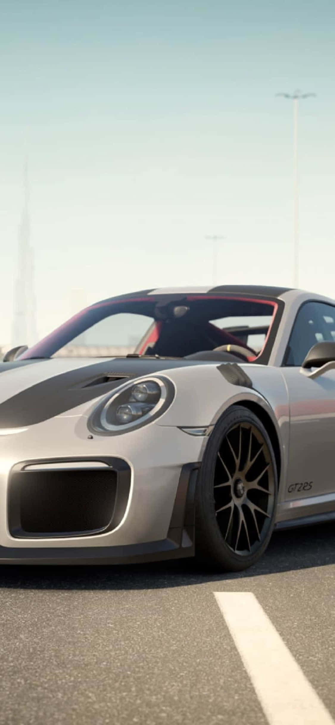 保時捷 911 iPhone X 炫酷《Forza Motorsport 7》背景 壁紙 — 一輛時尚的銀色保時捷911 GT2 RS，帶有黑色飾邊和紅色內飾，停在陽光明媚的道路上，遠處是城市天際線。