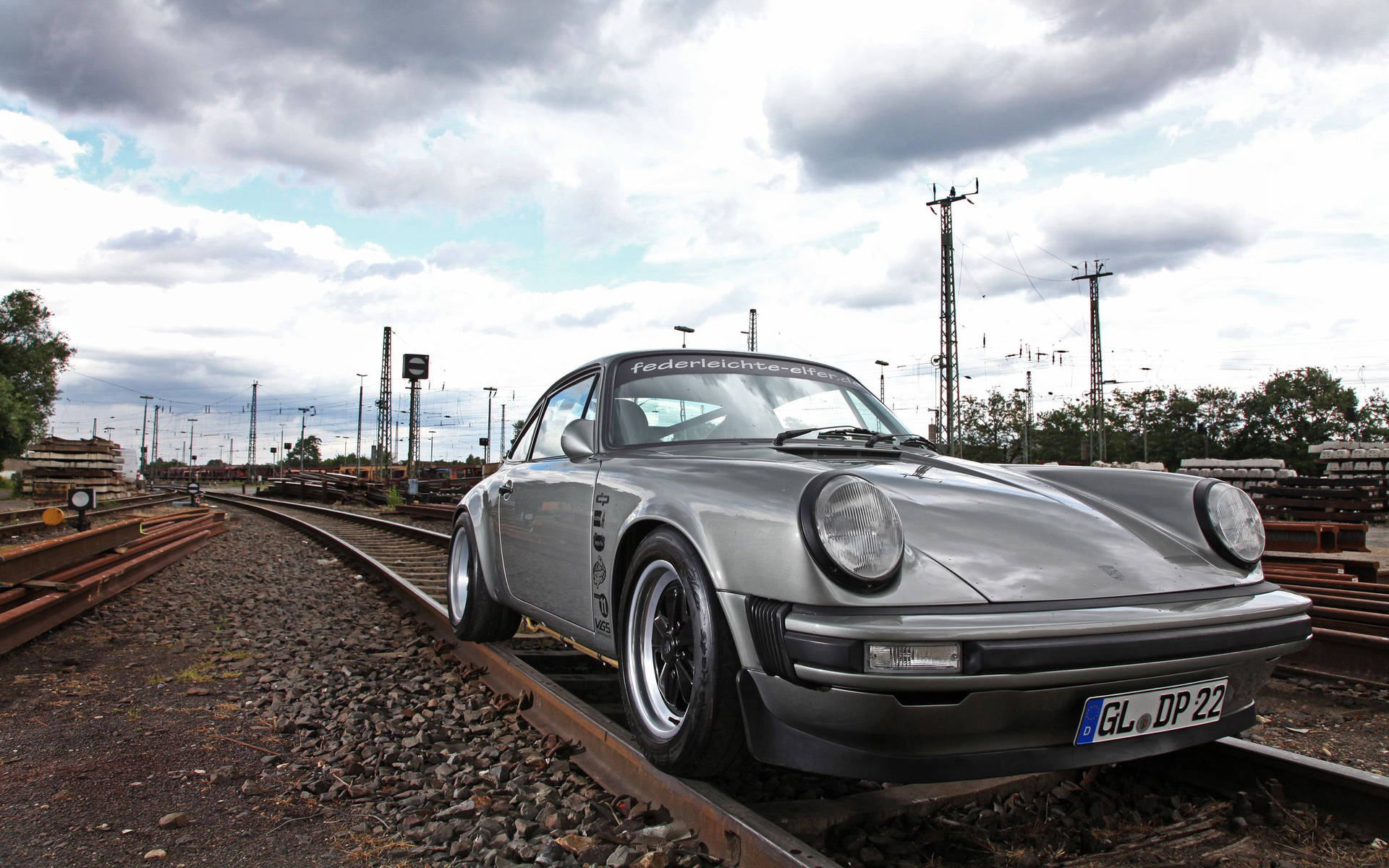銀色經典保時捷911停泊在火車軌道上，背景為多雲天空。