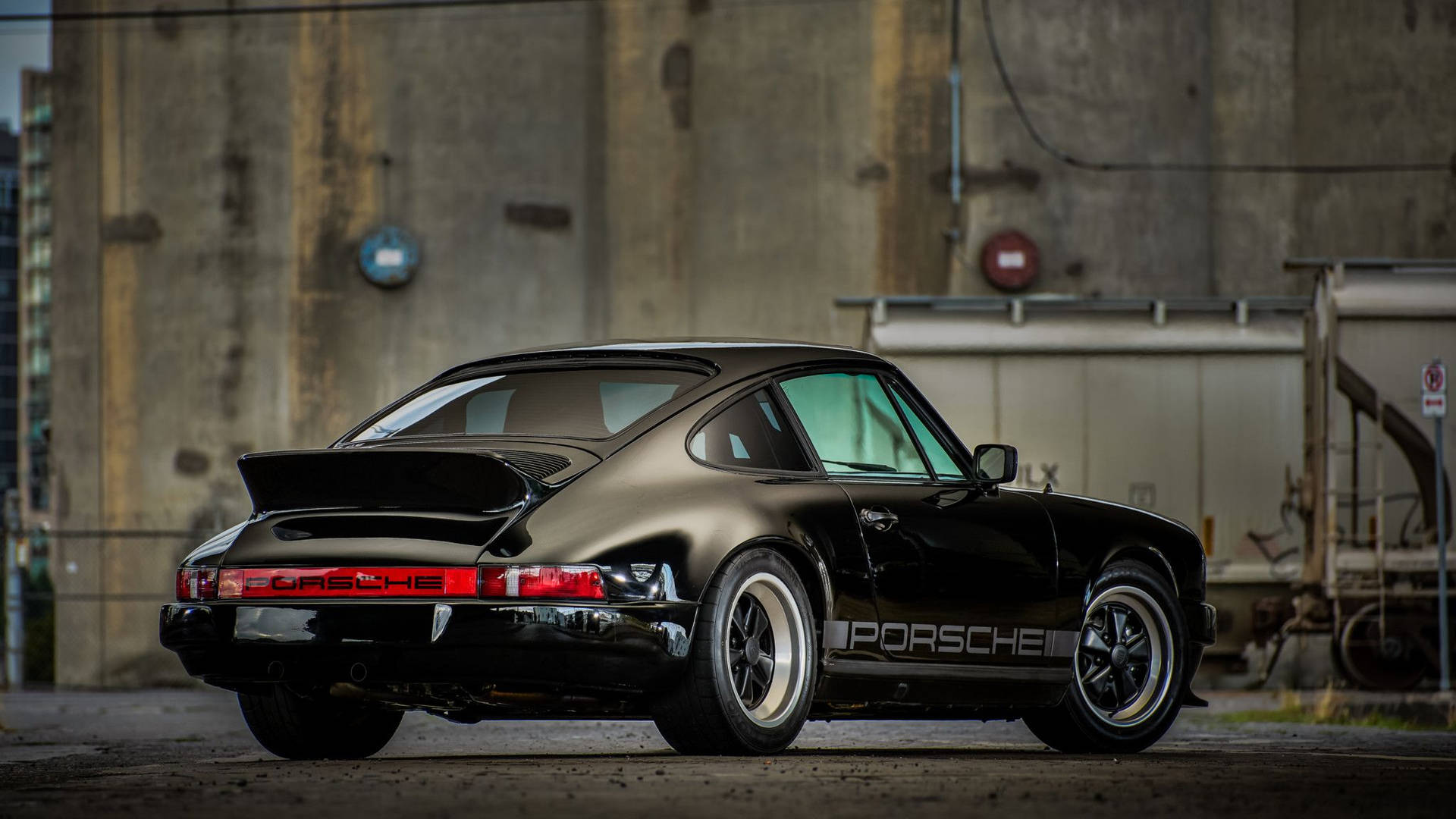 黑色保時捷911 Turbo，帶有銀色條紋，停在混凝土倉庫前。