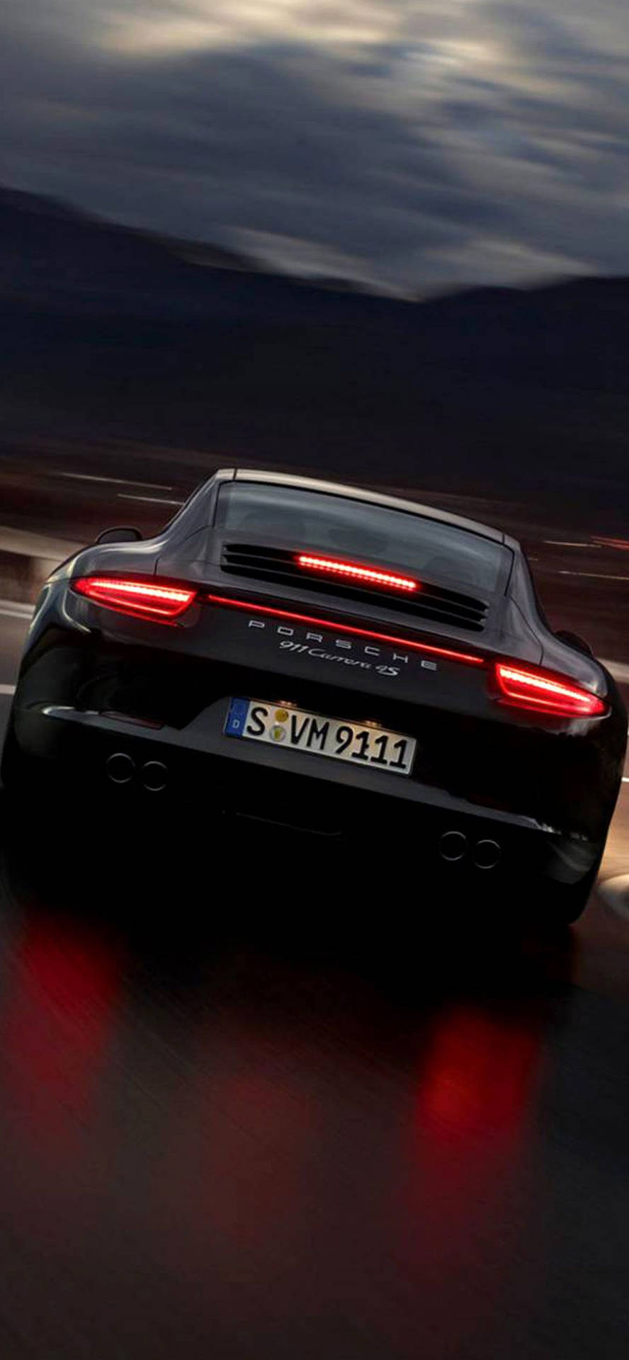 黑色保時捷911 GT3 RS在黃昏時加速駛離，紅色尾燈在潮濕路面上反射。