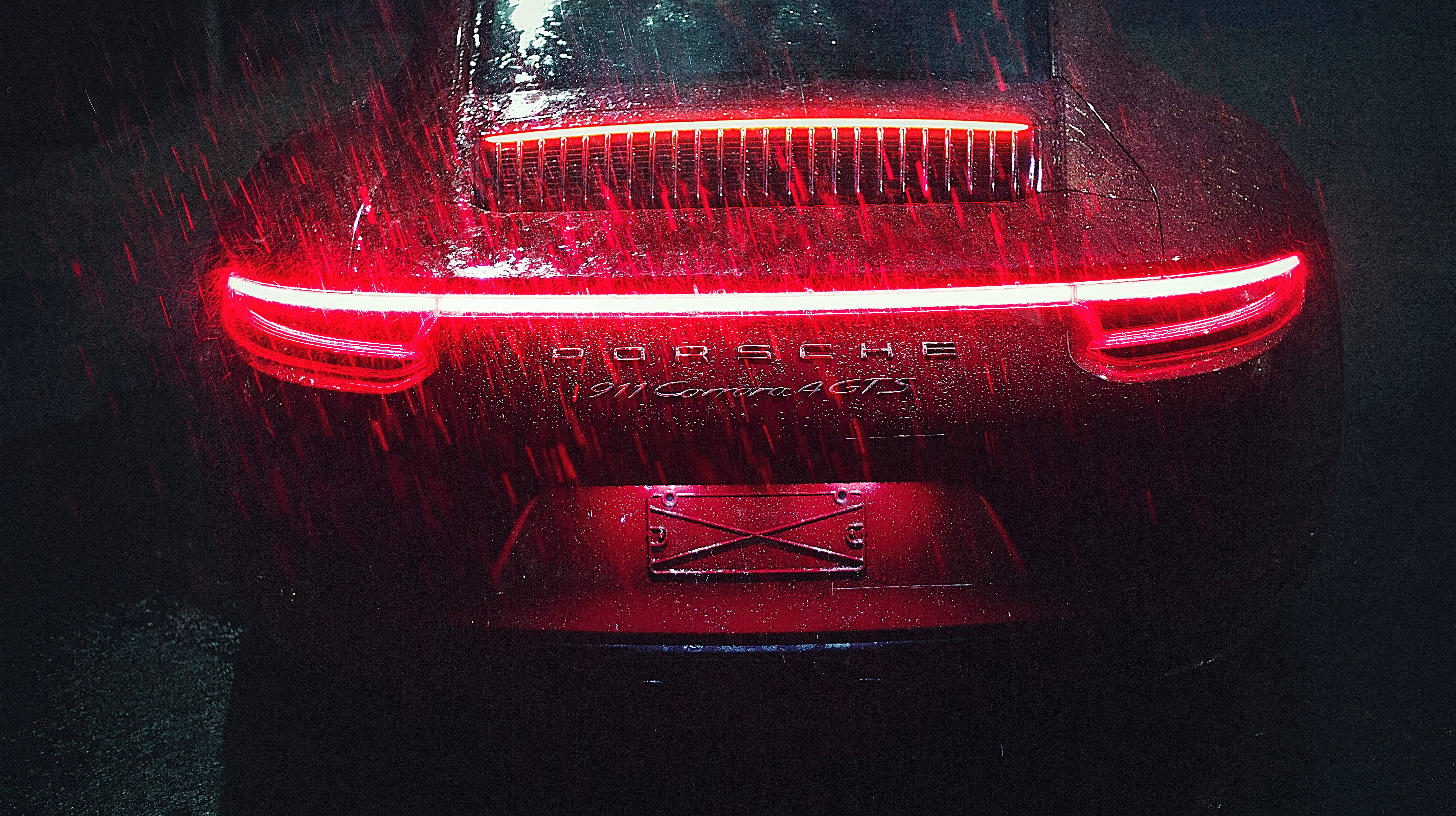 保時捷911尾燈 壁紙 — 一輛紅色保時捷911 Carrera GTS在夜間大雨中閃爍著鮮豔的尾燈。