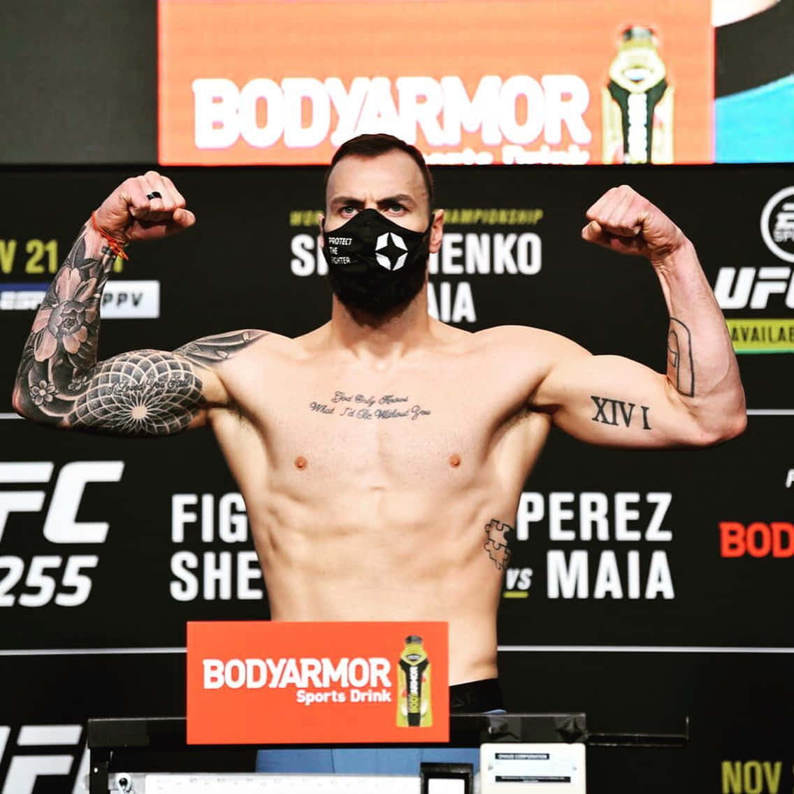 UFC拳手在稱重時彎曲手臂，戴著黑色口罩和紋身