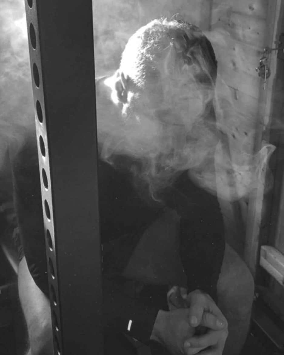 一個男人在室內吸煙，煙霧在他的臉和手周圍旋轉。