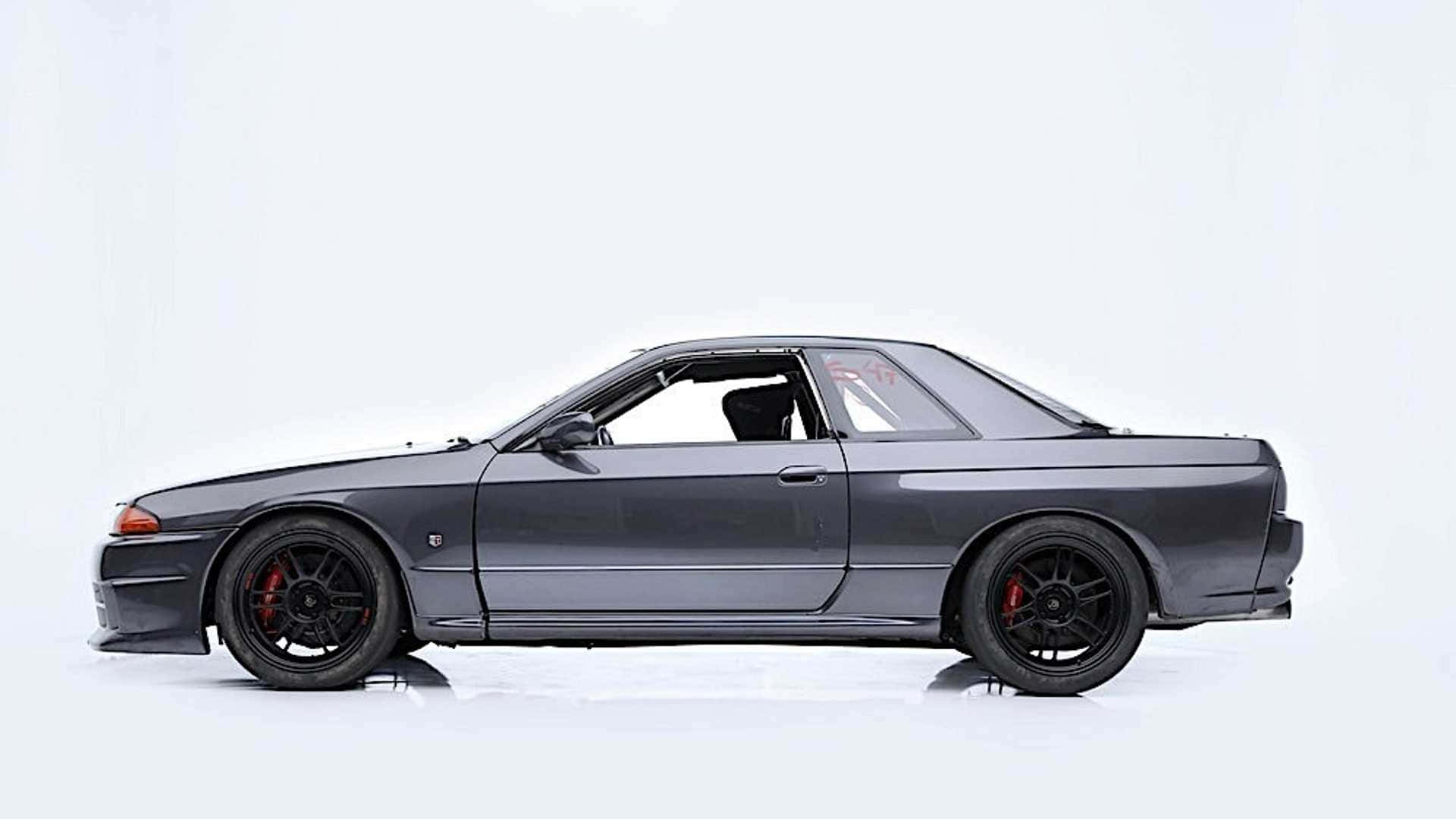 深灰色日產Skyline GT-R，配備黑色輪圈和紅色制動卡鉗，在白色工作室中。