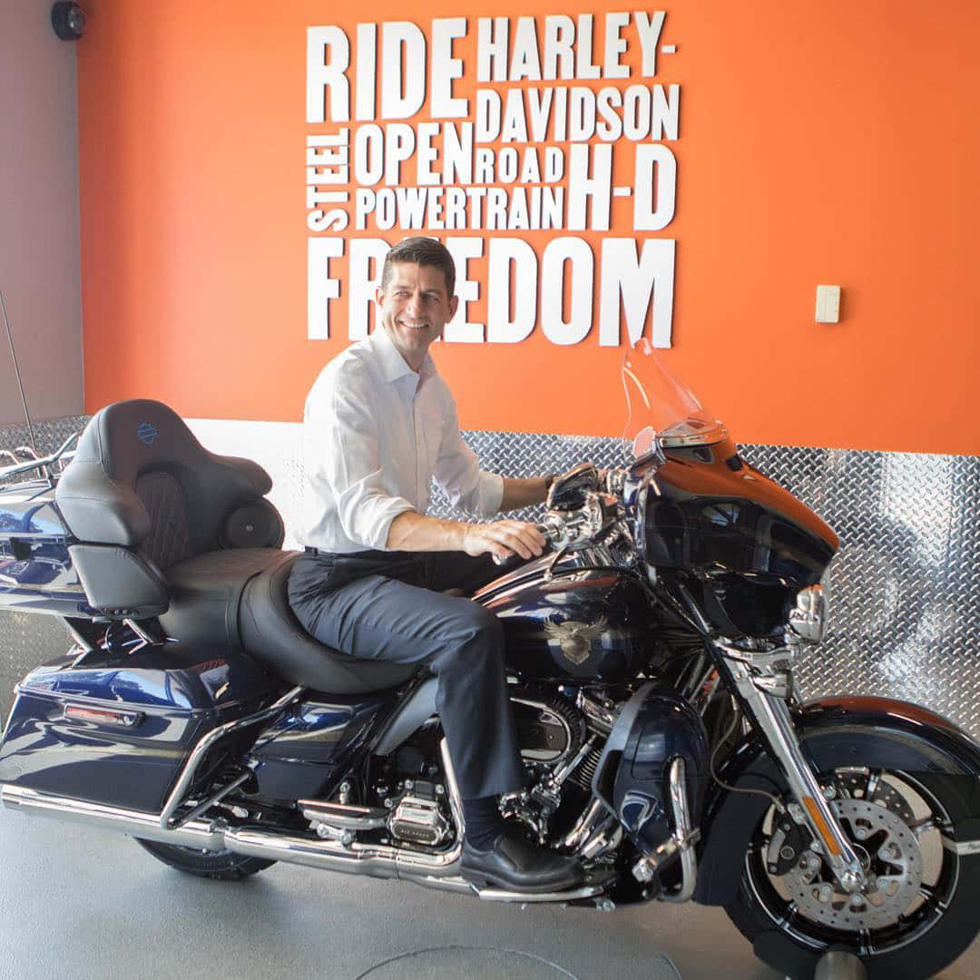 男子微笑著坐在黑色Harley-Davidson電單車上，身處有橙色牆壁文字的陳列室。