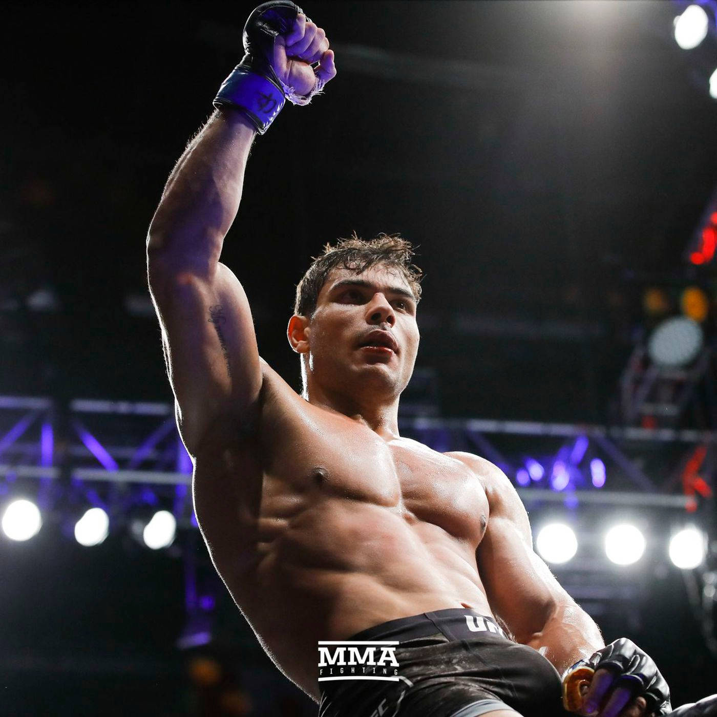 保羅·科斯塔勝利姿態 壁紙 — 一位肌肉發達的MMA拳手在明亮的場館燈光下，勝利後高舉戴著手套的拳頭。