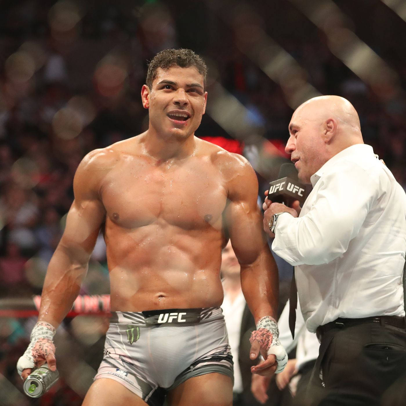 保羅·科斯塔等待勝利宣告 壁紙 — 一名汗流浹背的UFC拳手在勝利中閃耀，一名光頭記者在擁擠的競技場中將麥克風靠近他的肩膀。