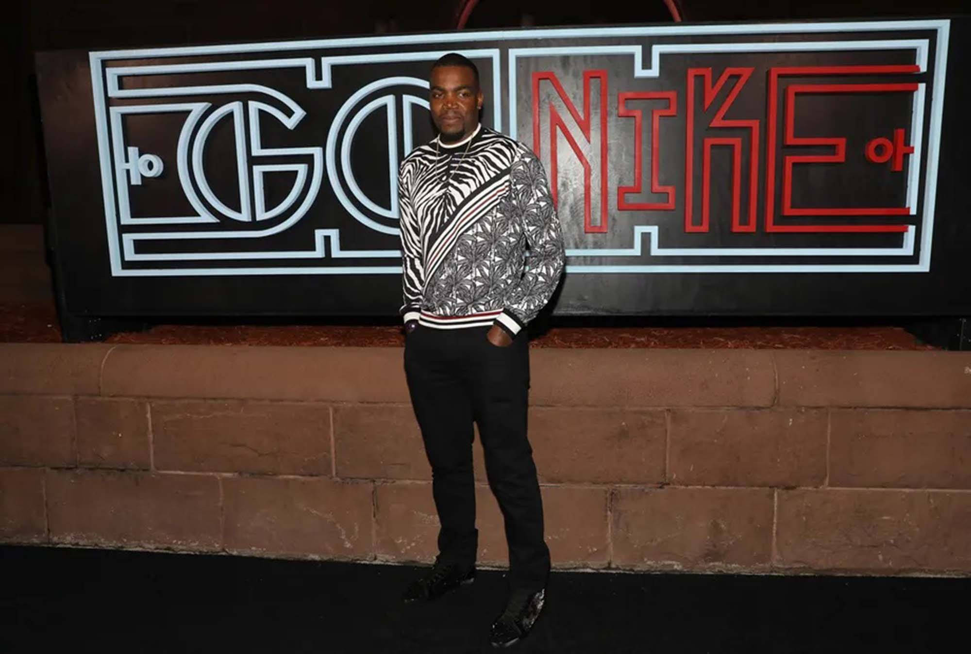 保羅·米利斯áp GQ x Nike活動 壁紙 — 一名男子穿著大膽的黑白圖案毛衣，在夜間自信地站在發光的「GO NIK」標誌前。