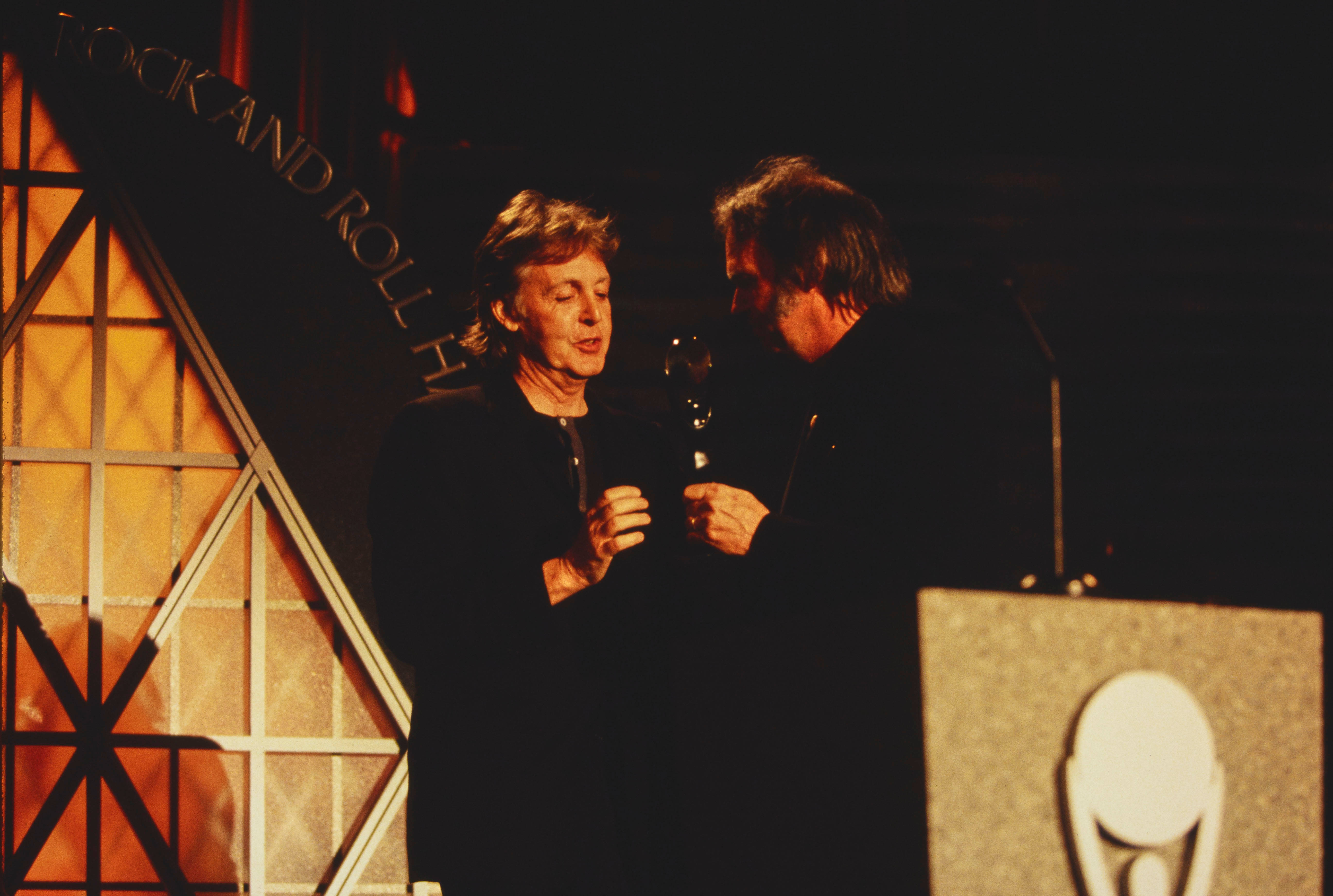 Paul McCartney Hall Of Fame 壁紙 — 保羅·麥卡尼在搖滾名人堂入駐典禮上，在溫暖的聚光燈下於舞台上接受獎盃。