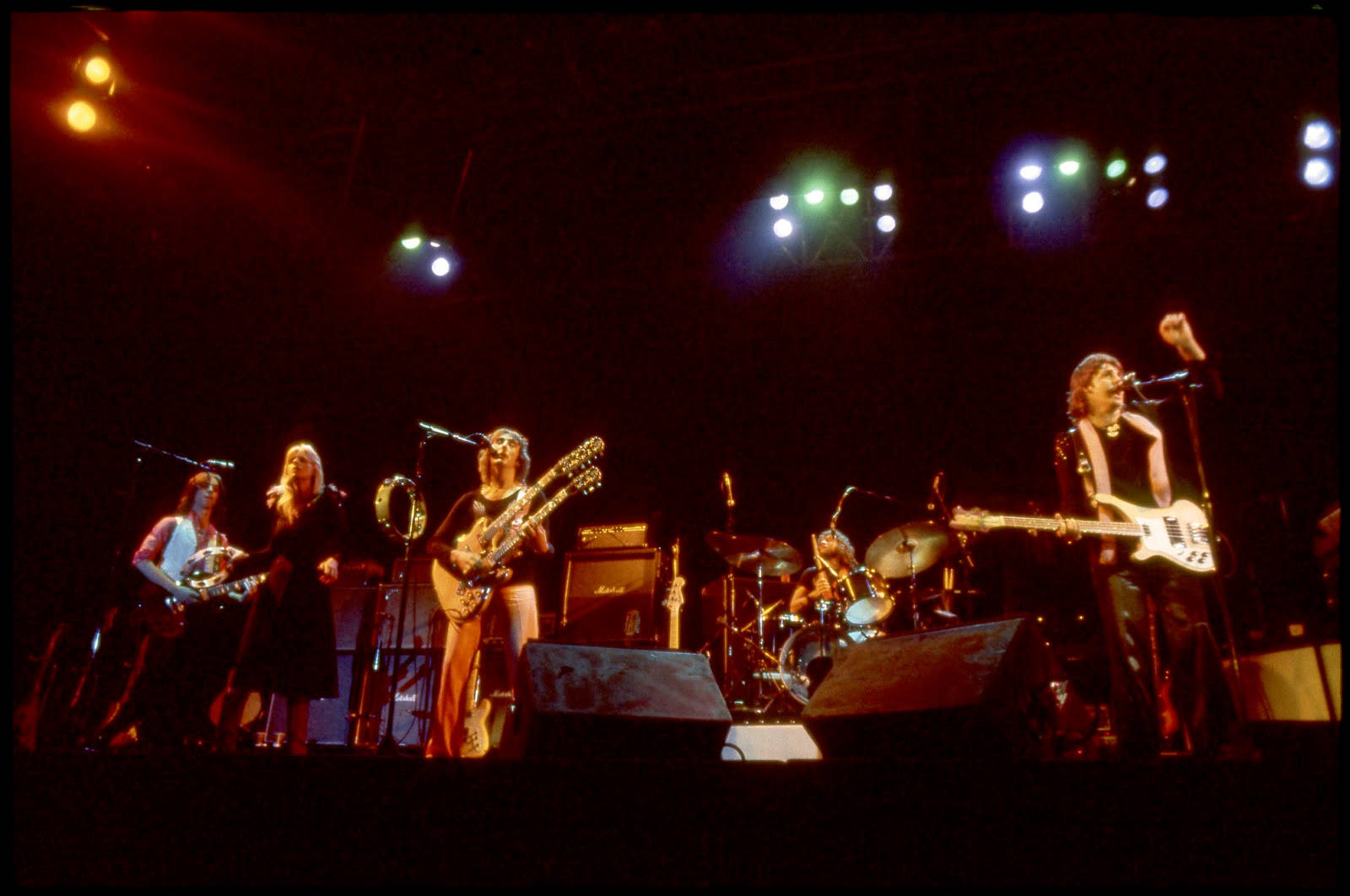 保羅·麥卡特尼與 Wings 1974年西雅圖現場演出壁紙 壁紙 — 一支復古搖滾樂隊在昏暗的舞台上，在彩色聚光燈下，用結他、鼓和咪高峰表演。