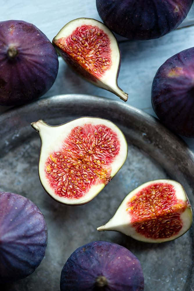 Purple Figs 桌布 壁紙 — 俯拍成熟紫色無花果切開後露出多汁粉紅色內部，放在質樸金屬托盤上的照片。