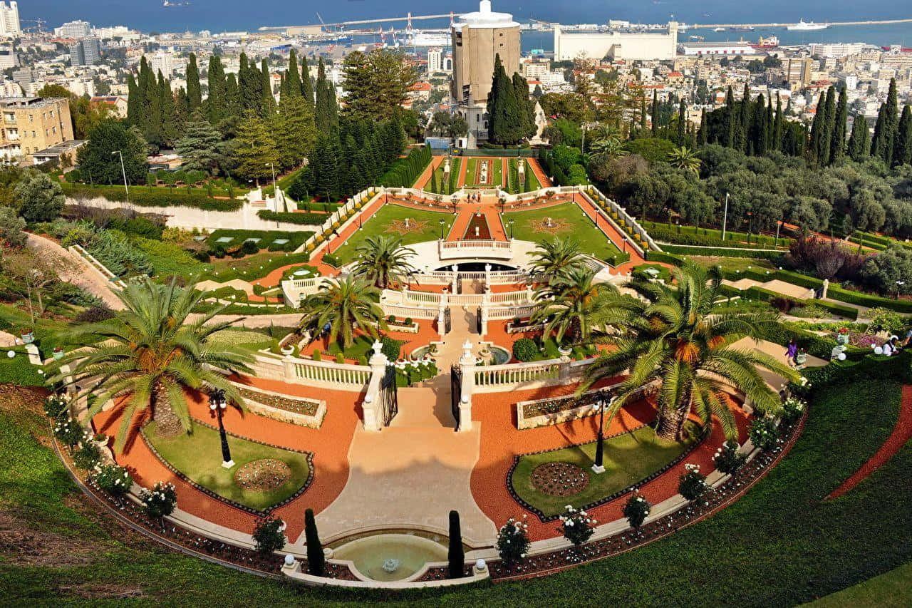 Israel 桌布 壁紙 — 俯瞰一個宏偉的梯田花園，內有棕櫚樹、噴泉和幾何圖案小徑，遠眺沿海城市和港口。