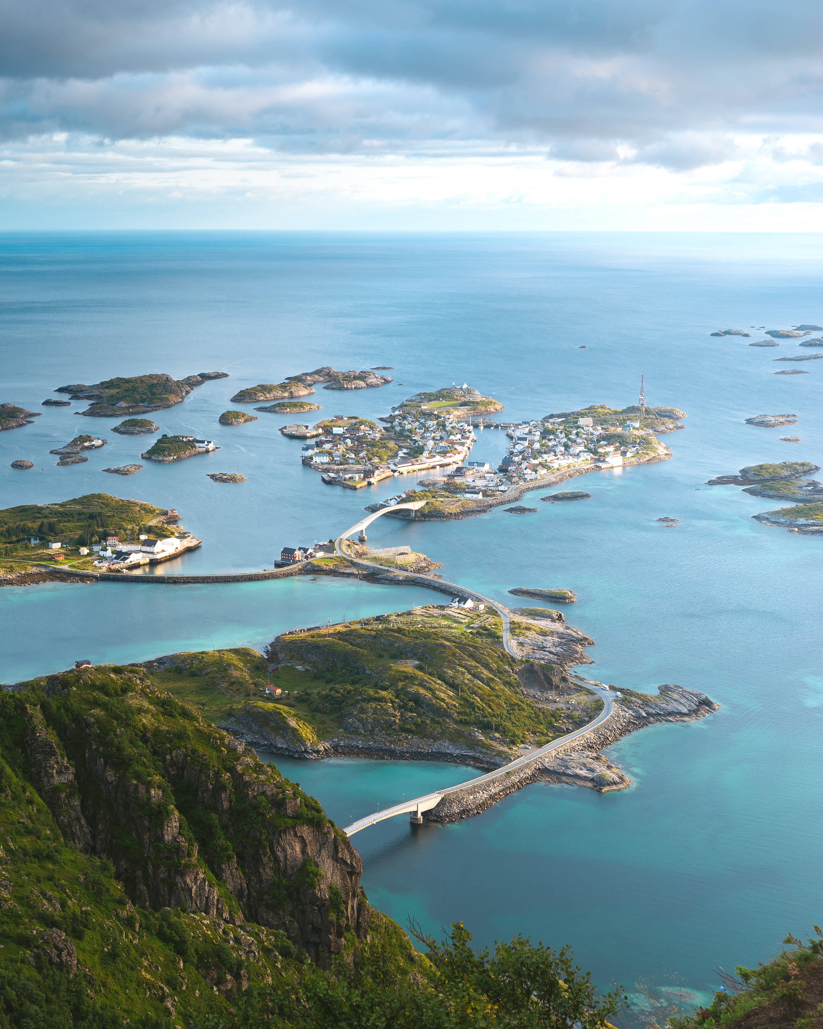 Norway 桌布 壁紙 — 俯瞰一個沿海村莊，坐落在碧綠海水和綠色島嶼之間，由蜿蜒的道路和橋樑連接。