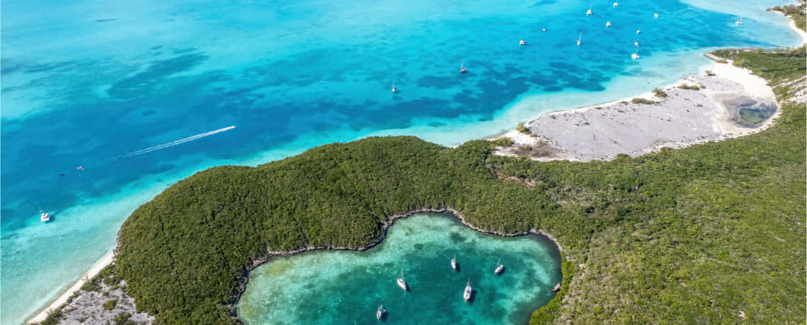 Bahamas Island 桌布 壁紙 — 俯瞰一個鬱鬱蔥蔥的綠色島嶼，擁有碧綠的海水和沿著白色沙灣停泊的帆船。