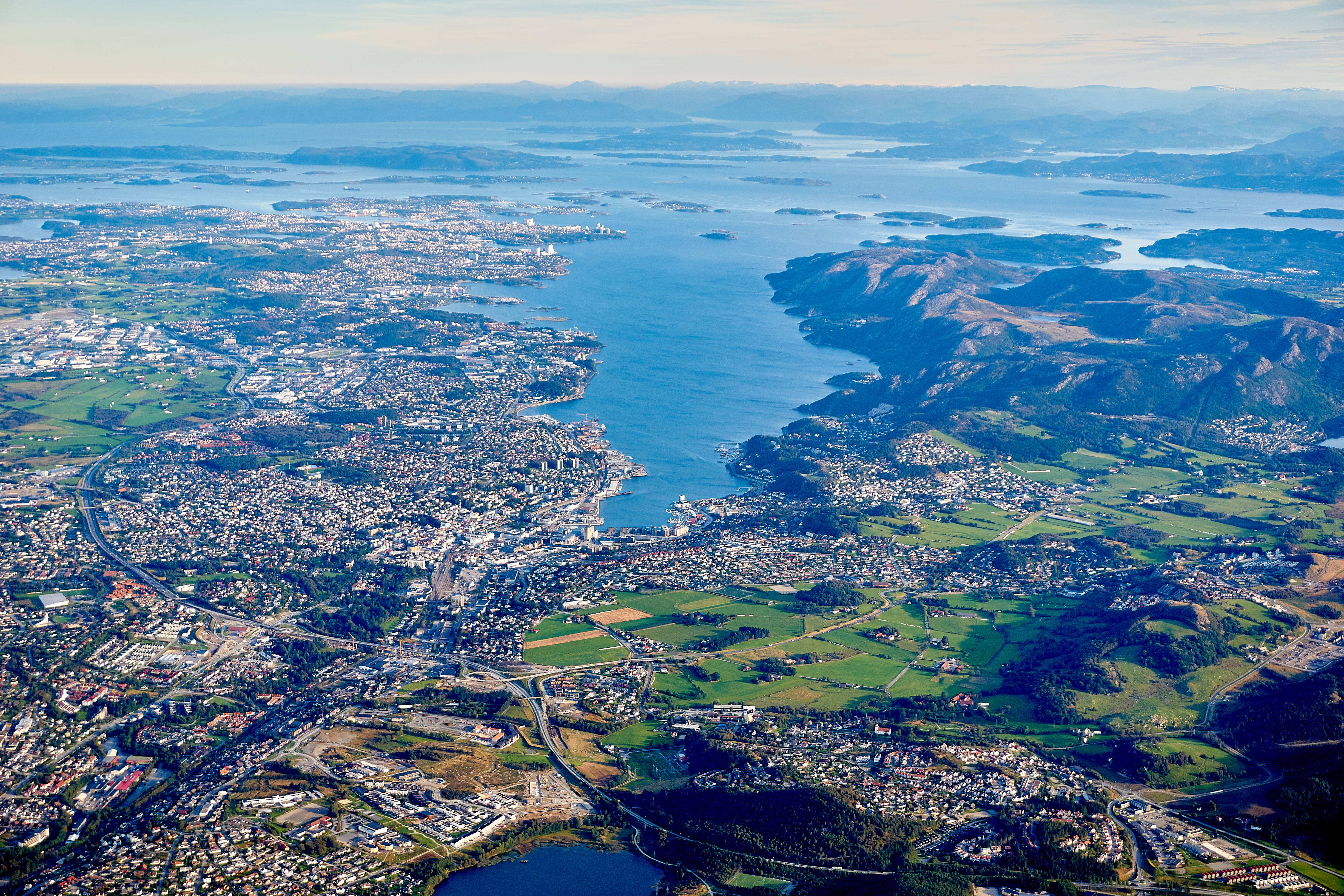 Norway 桌布 壁紙 — 俯瞰一座坐落於翠綠山丘與廣闊藍色峽灣之間的海岸城市，天空晴朗。