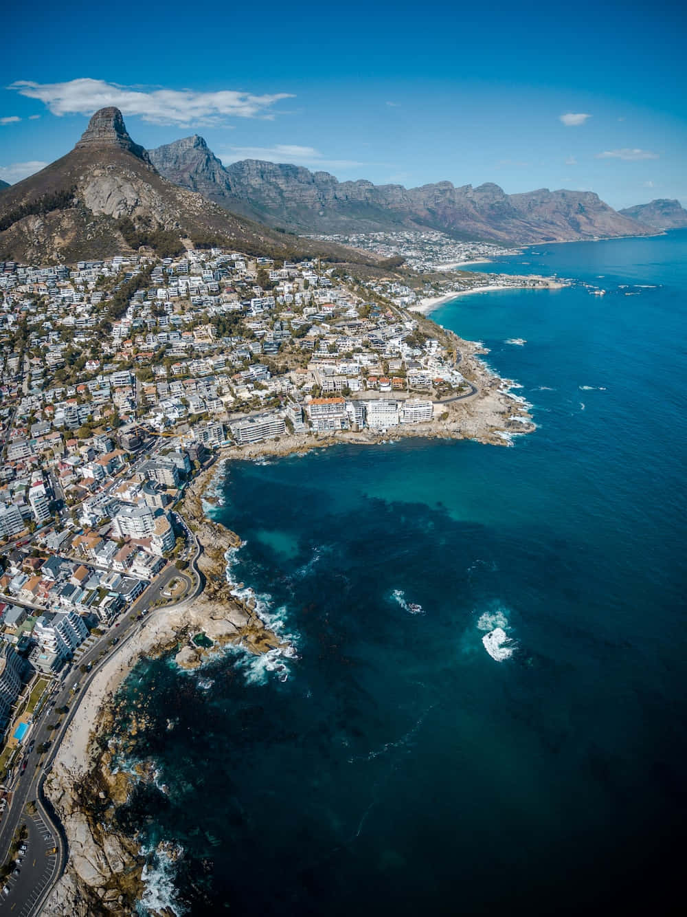 South Africa 桌布 壁紙 — 俯瞰一座沿海城市，坐落於崎嶇山脈與碧綠海洋之間，白色建築與蜿蜒道路清晰可見。