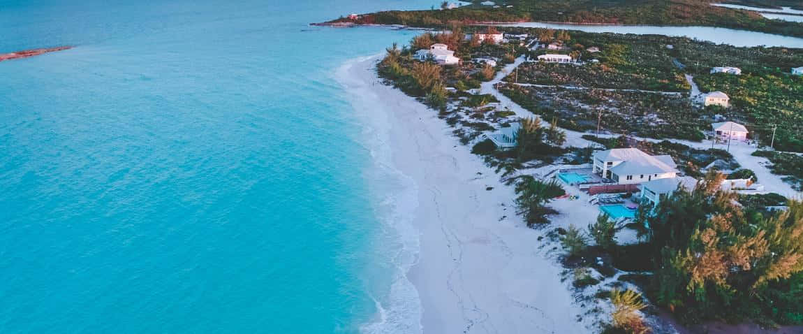 Bahamas Island 桌布 壁紙 — 俯瞰圖：碧綠海水輕拍純白沙灘，沙灘旁散落著白色房屋和綠植。