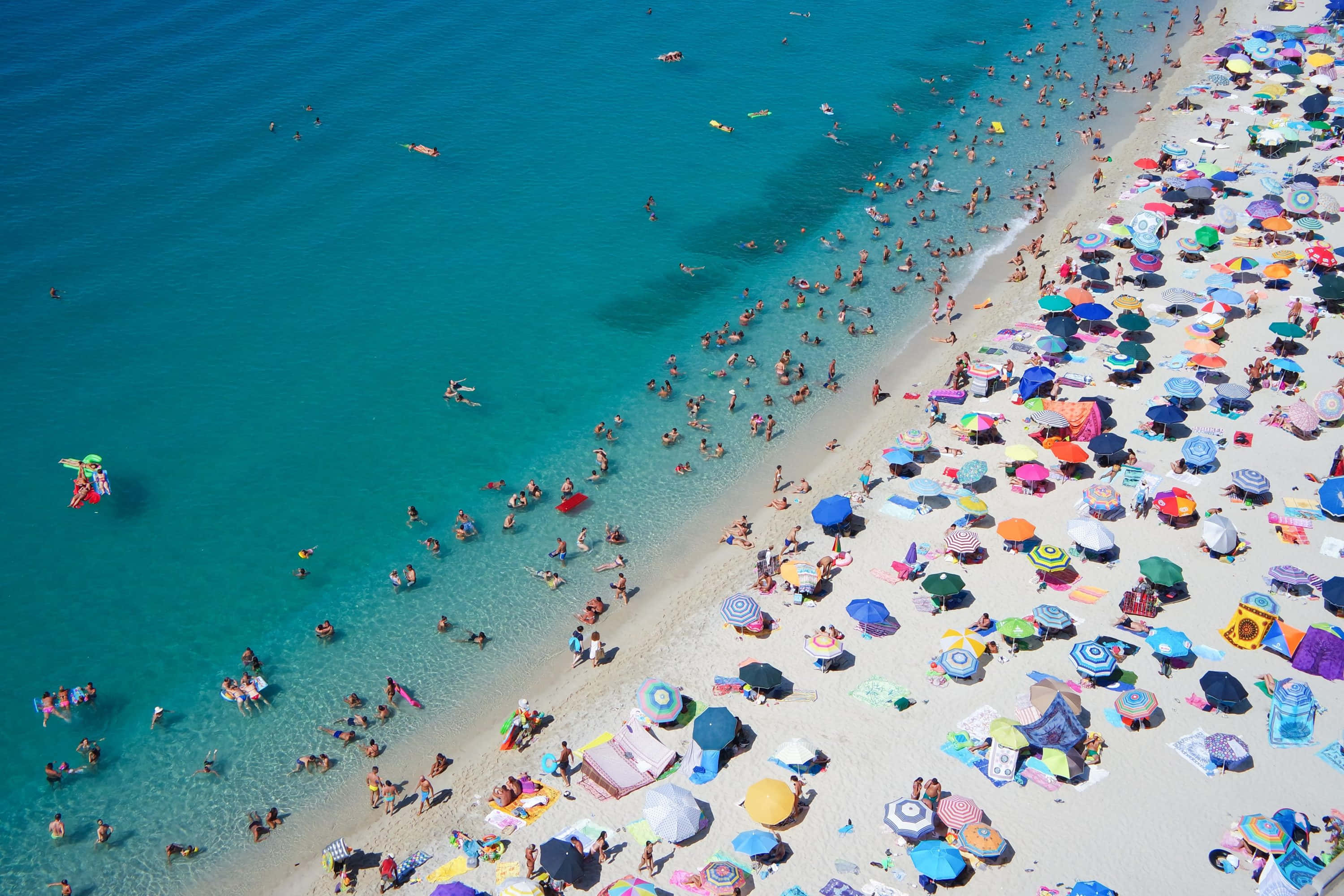 Italian Beach 桌布 壁紙 — 俯瞰擠滿人的沙灘，碧綠海水與彩虹色遮陽傘點綴著沙灘。