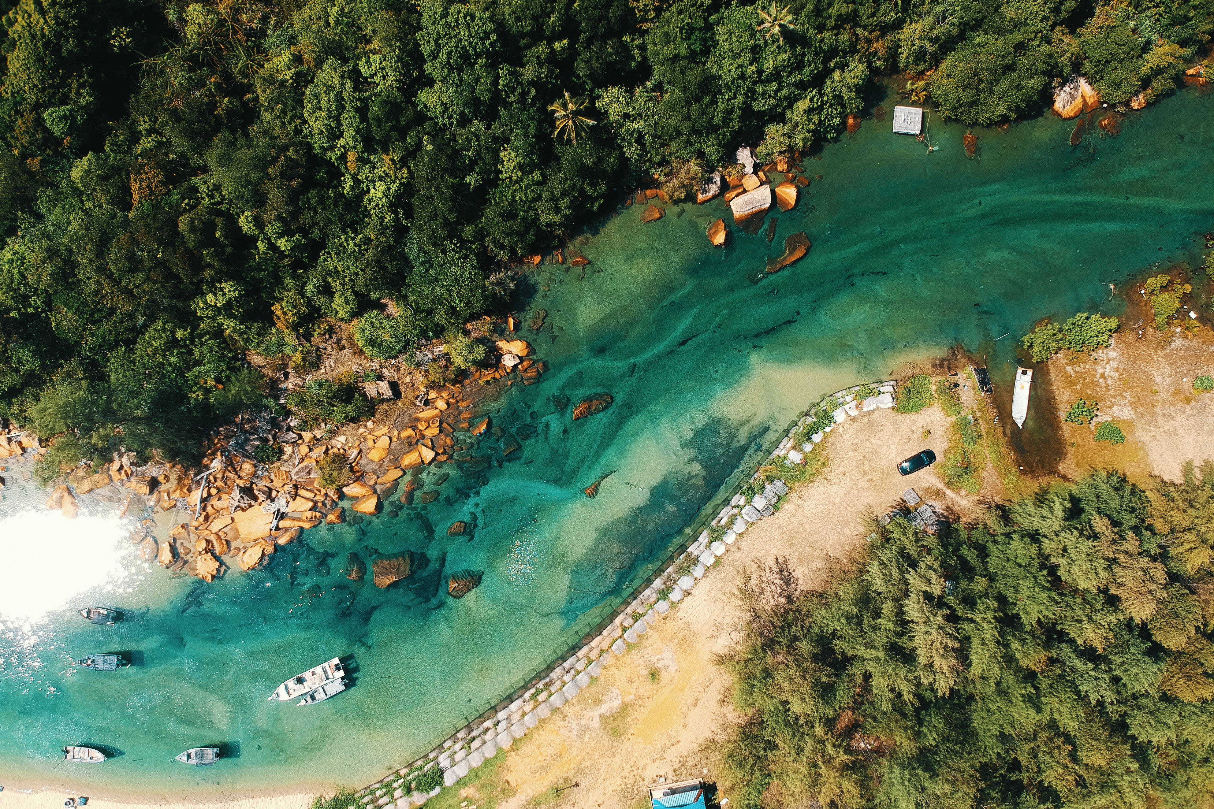 俯瞰河景 壁紙 — 鳥瞰圖，碧綠海水擁抱著沙灘海灣，兩旁是茂密的綠色叢林和散落的船隻。
