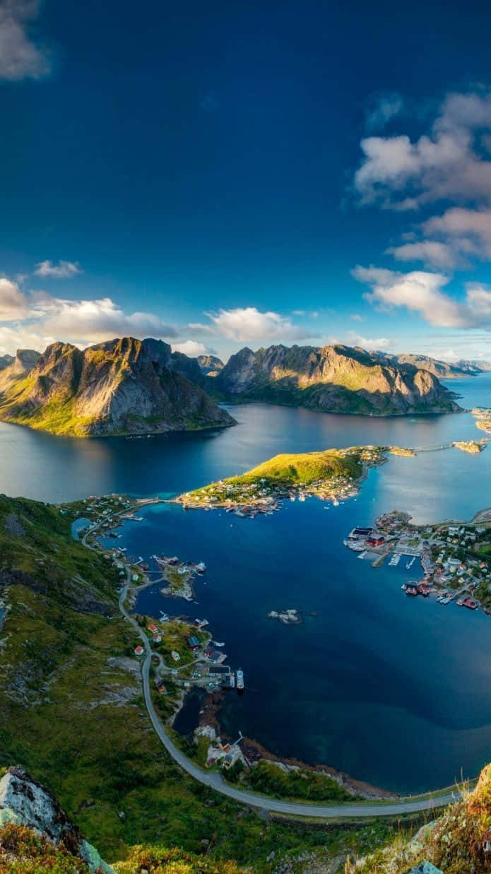 Norway 桌布 壁紙 — 俯瞰蜿蜒海岸公路緊貼深藍色峽灣，四周是崎嶇的綠色山脈，明亮的藍天中散佈著雲朵。