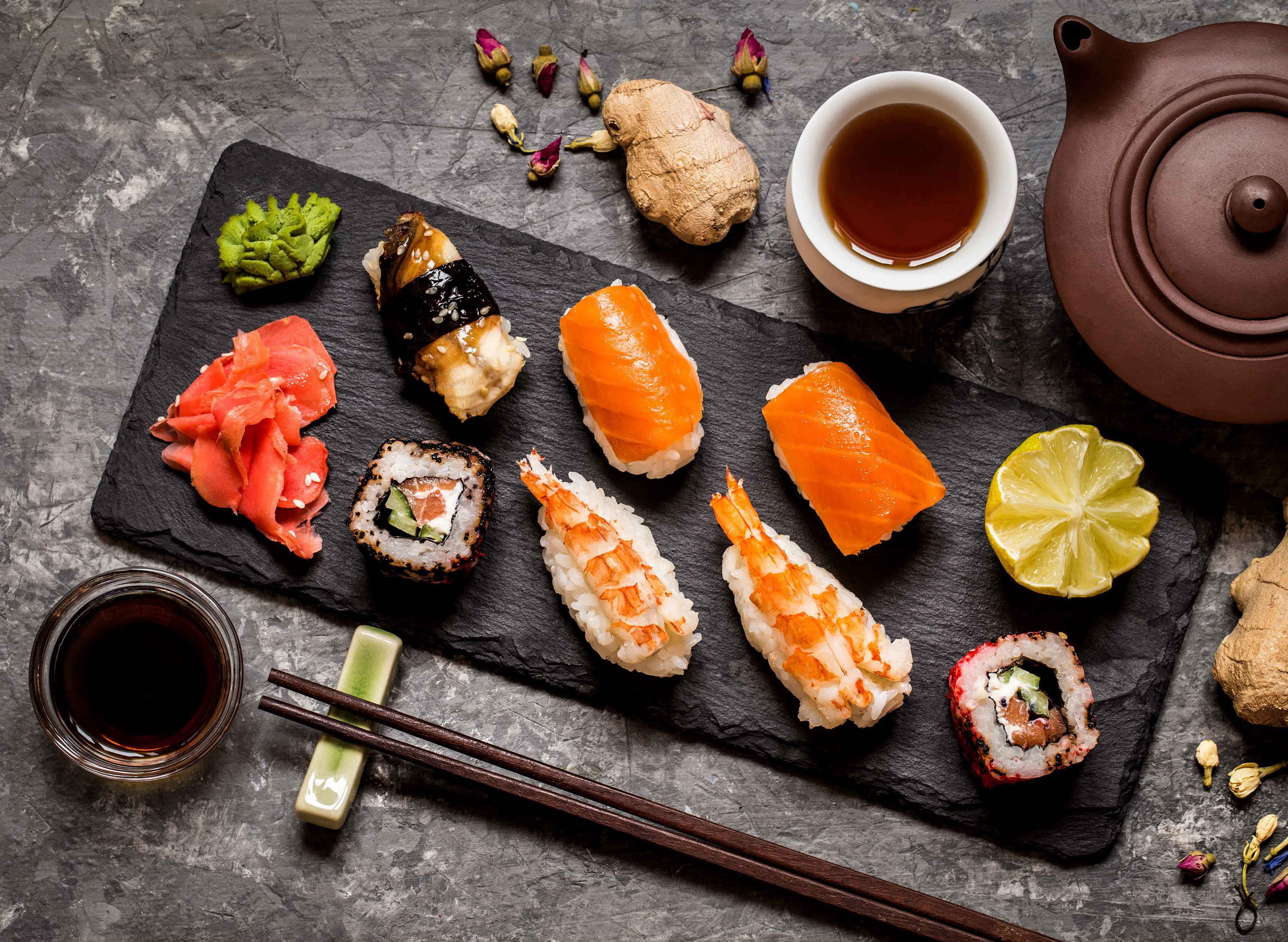 Sushi 桌布 壁紙 — 俯瞰視角下，各種壽司片排列在黑色石板上的醬油、生薑和茶具旁。