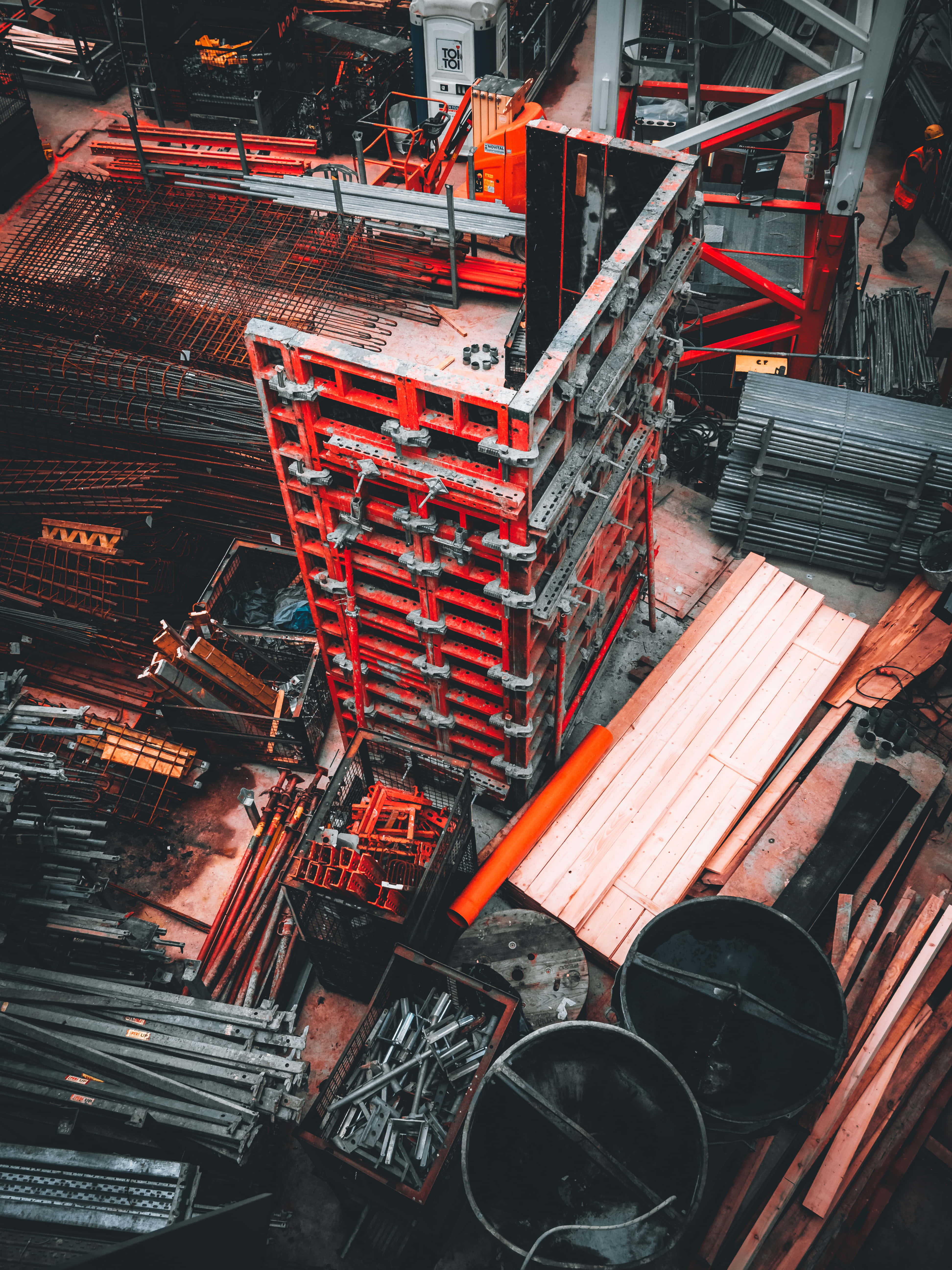 Civil Engineering 桌布 壁紙 — 俯瞰雜亂的建築工地，紅色金屬棚架聳立在鋼筋和木板堆之上。