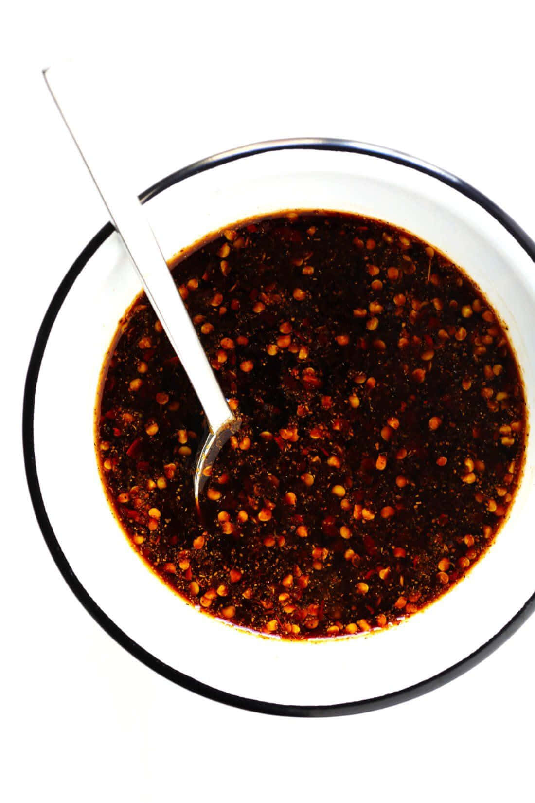 Szechuan Sauce 桌布 壁紙 — 俯視一個白色碗，黑色邊緣，裝滿深色辣椒油和紅辣椒片，裡面放著一隻湯匙。