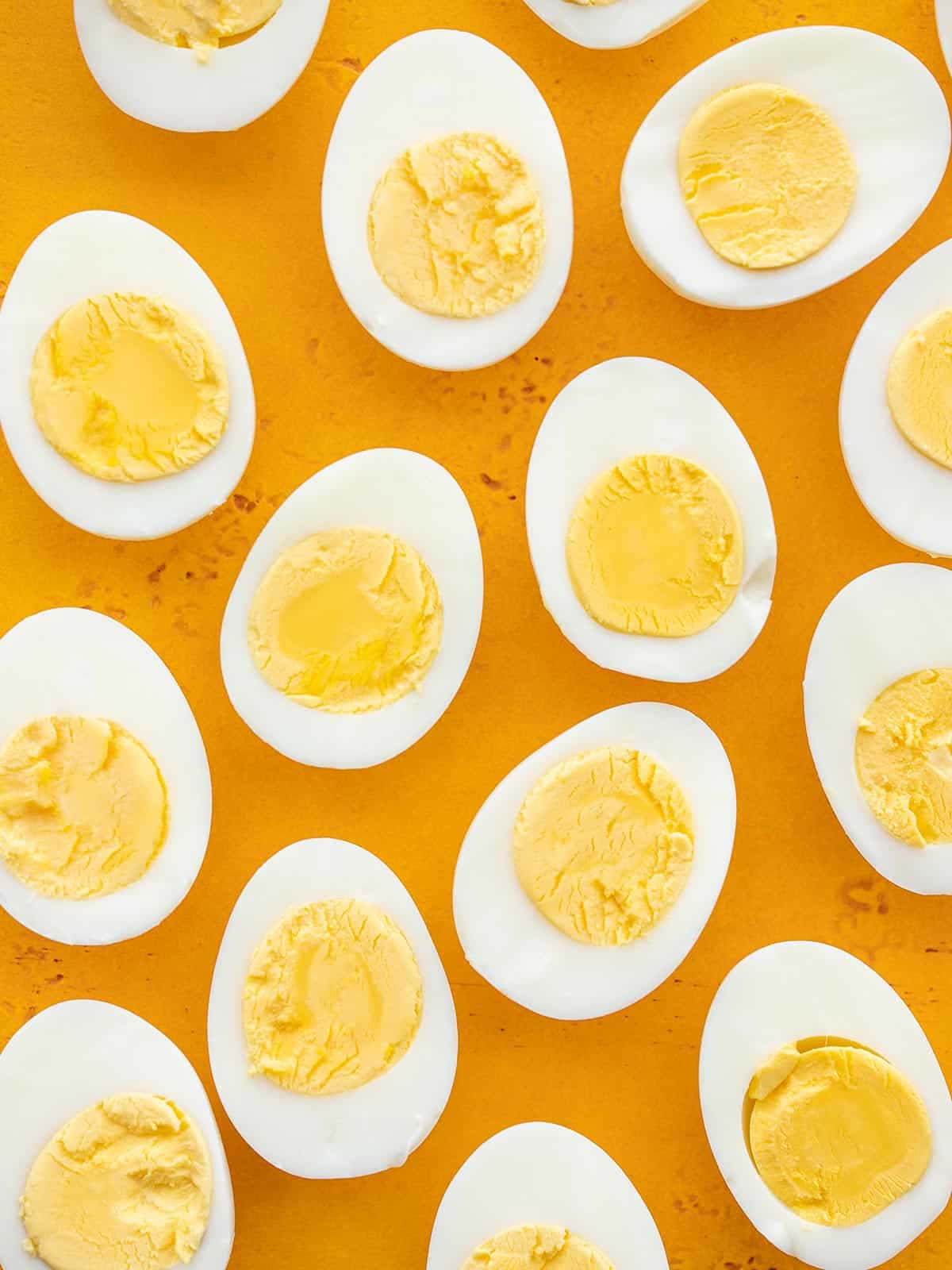 Eggs 桌布 壁紙 — 俯視圖：半邊水煮蛋配以奶油狀蛋黃，整齊排列在鮮豔的橙色表面上。
