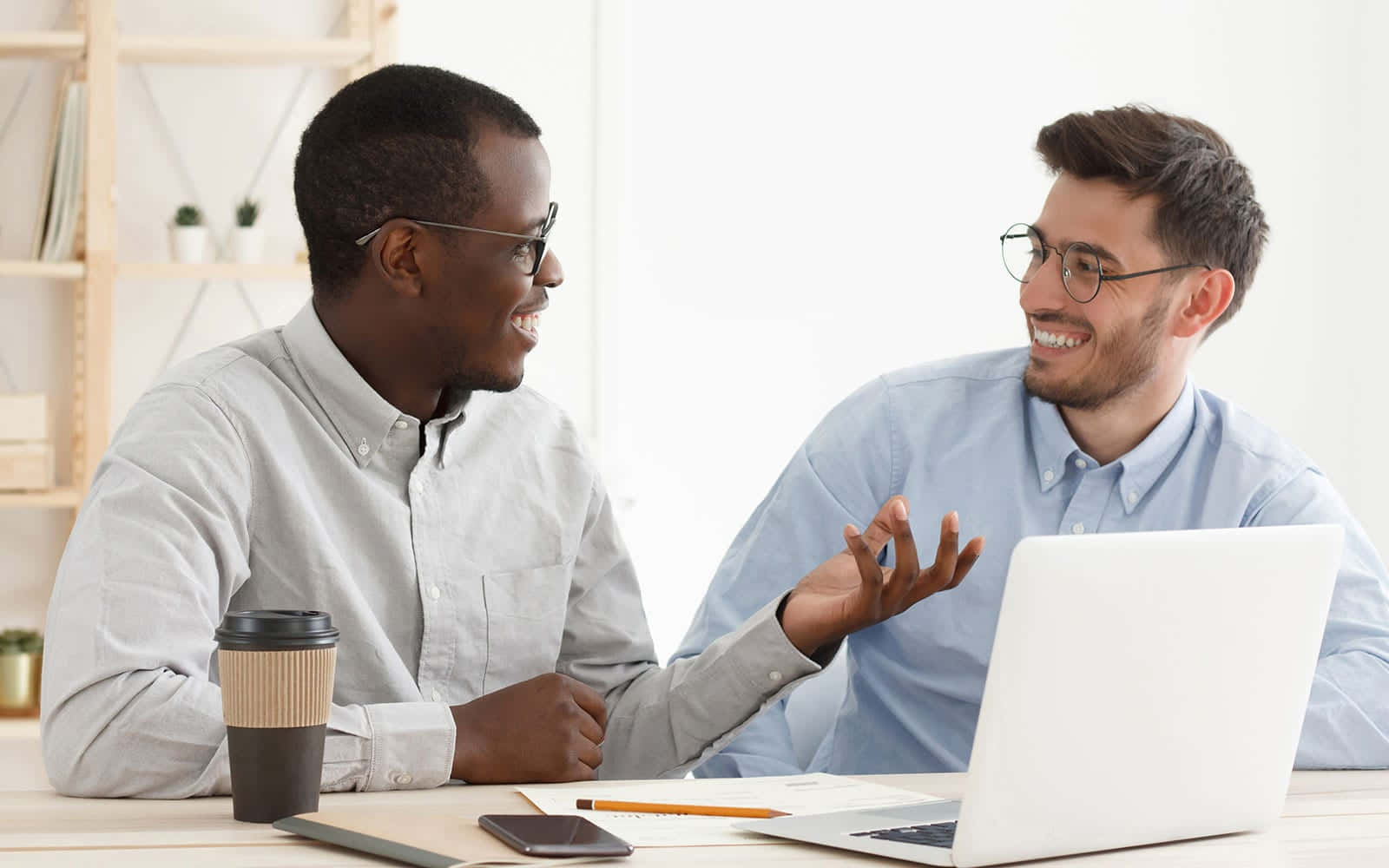 個人 Coaching 課程進行中 壁紙 — 兩位戴眼鏡的 smiling 男士在明亮現代的工作桌上，圍著手提電腦協作，旁邊有咖啡和筆記。