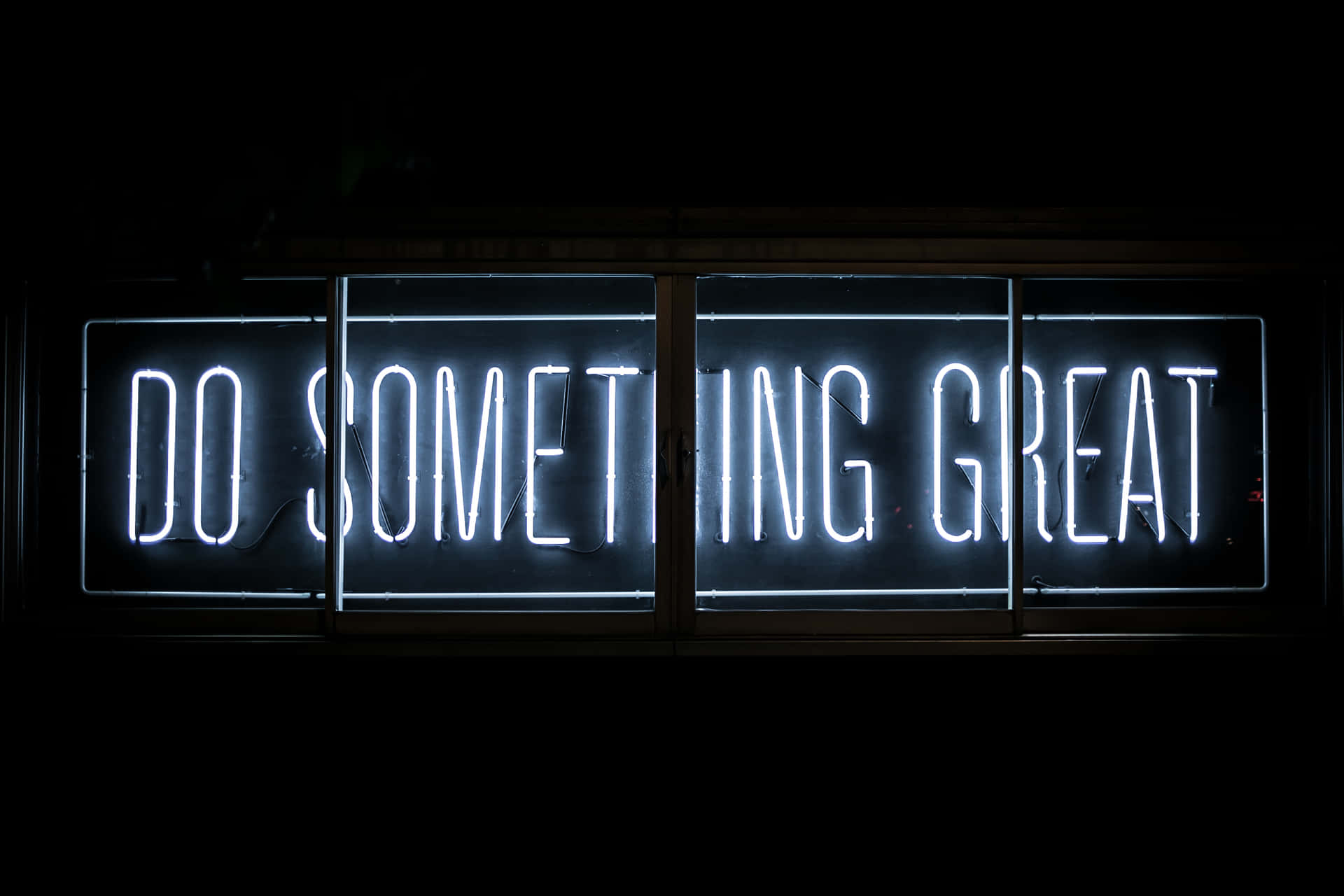 一個明亮的白色霓虹燈牌，上面寫著「DO SOMETHING GREAT」，背景為黑暗。
