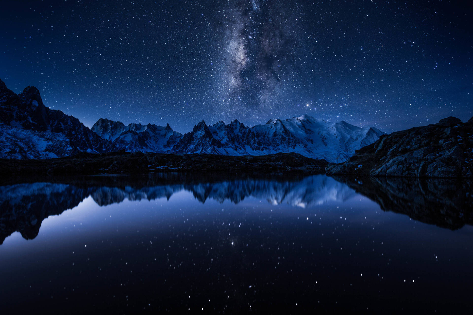 星空下積雪的山巒，夜晚倒映在平靜的湖面。
