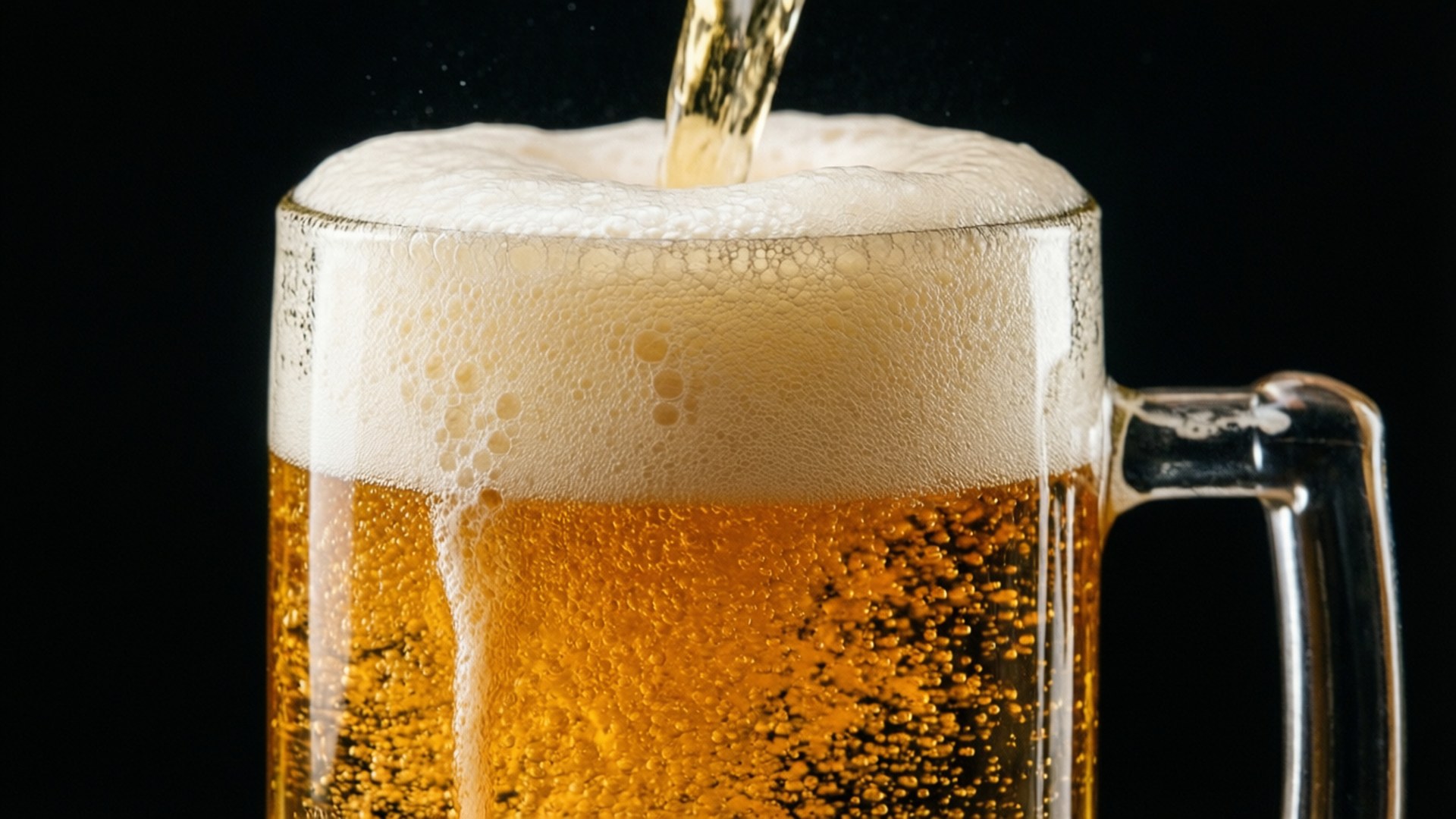 倒酒的德雷赫啤酒 壁紙 — 金色啤酒倒入玻璃杯，在黑色背景上形成泡沫頭。