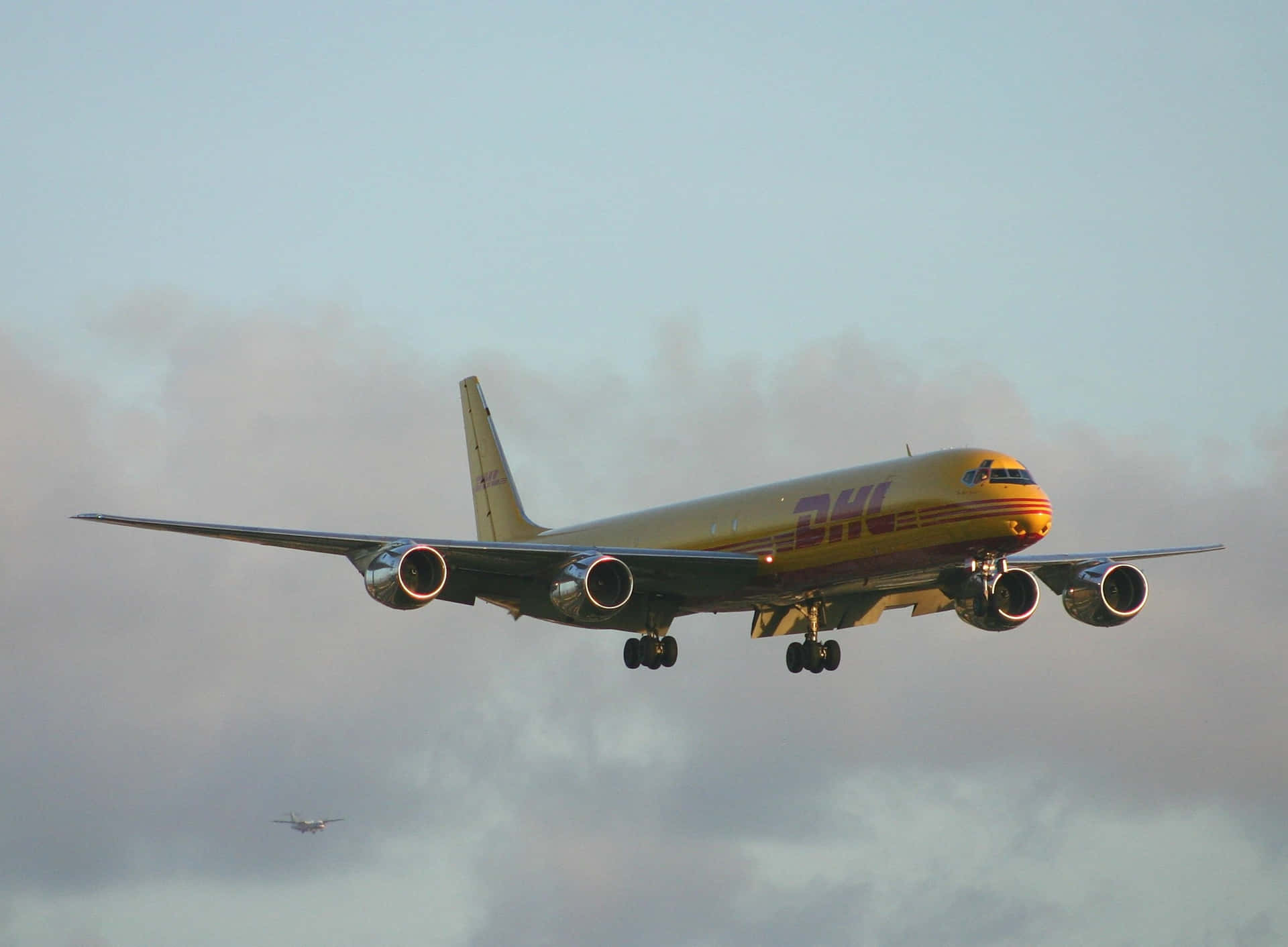 DHL貨機穿過多雲的天空降落，起落架放下。