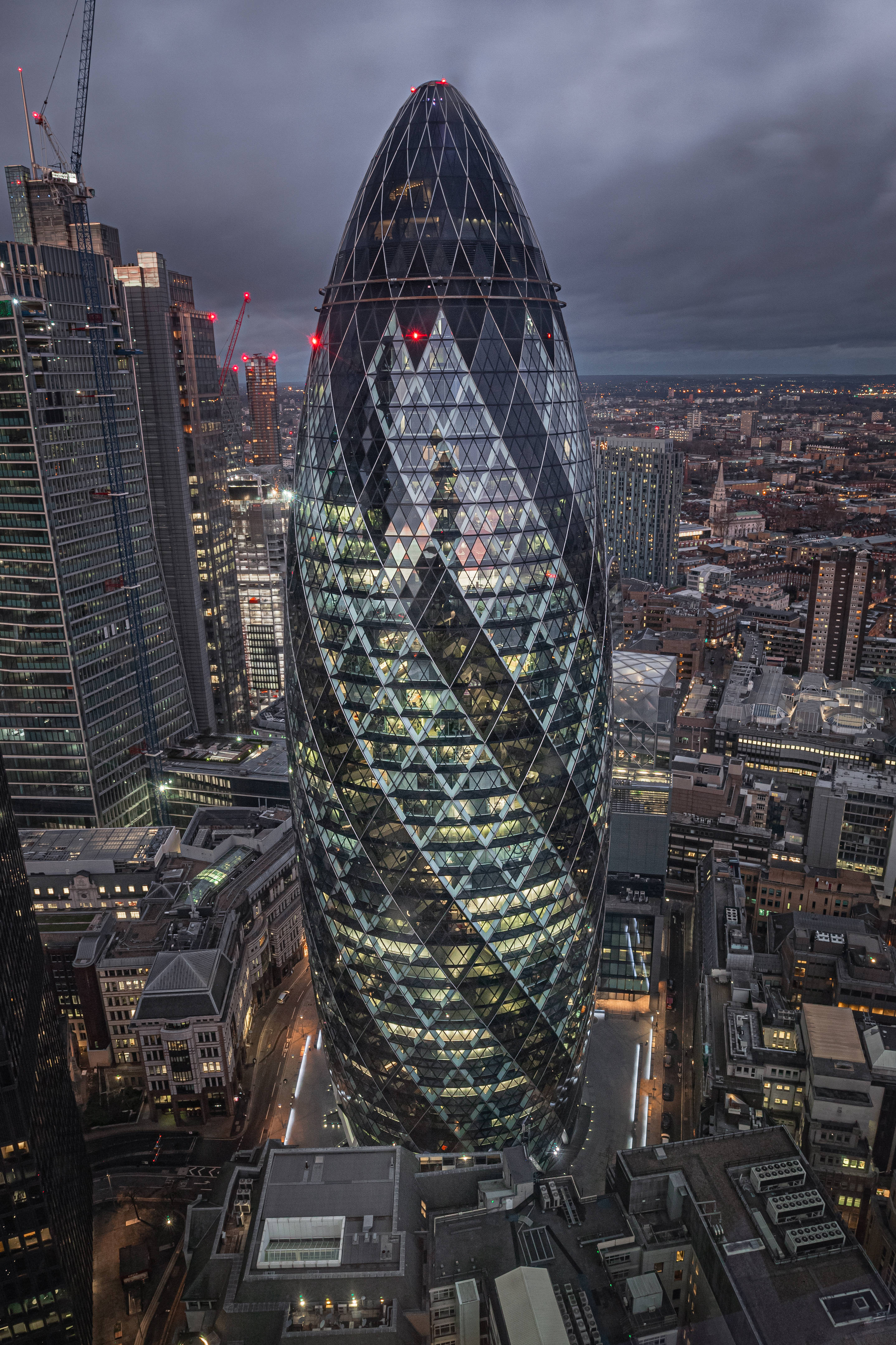 倫敦商業區的「The Gherkin」 壁紙 — 一座高聳的玻璃摩天大樓，具有獨特的彎曲形狀，在陰鬱的暮色天空下主導著密集的城市天際線。