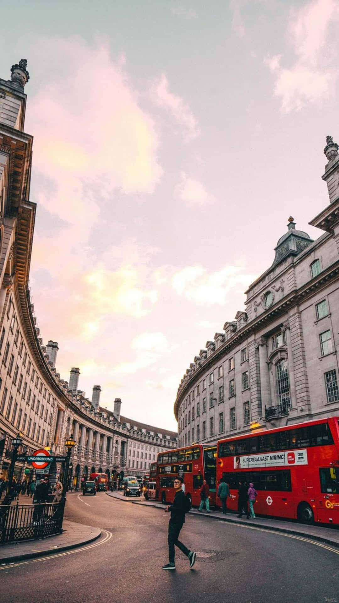 日落時分，一個人穿過彎曲的倫敦街道，有紅色雙層巴士和歷史建築。