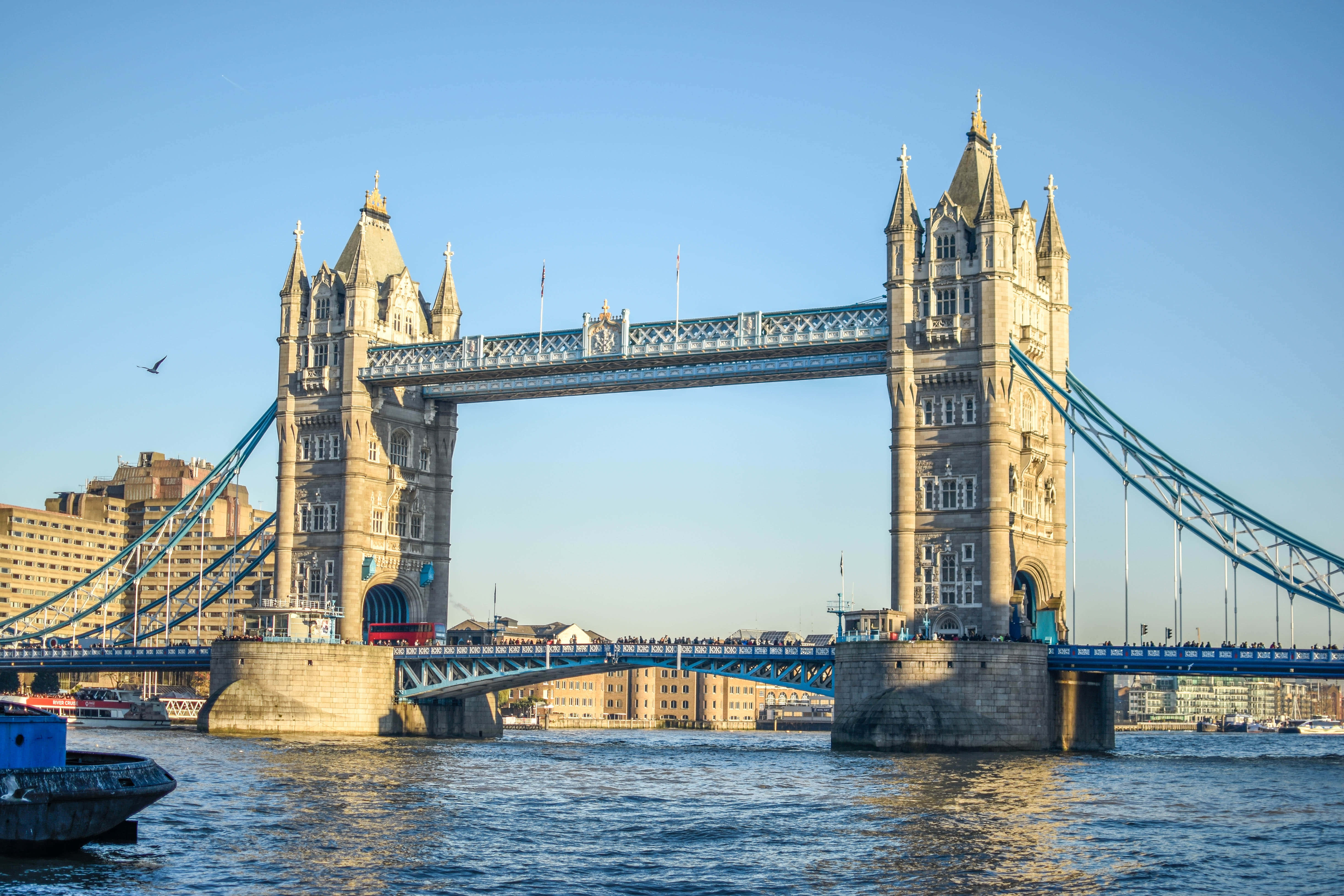 UK 桌布 壁紙 — 倫敦標誌性的塔橋在晴朗的藍天下雄偉地矗立在泰晤士河上，可見船隻和行人。