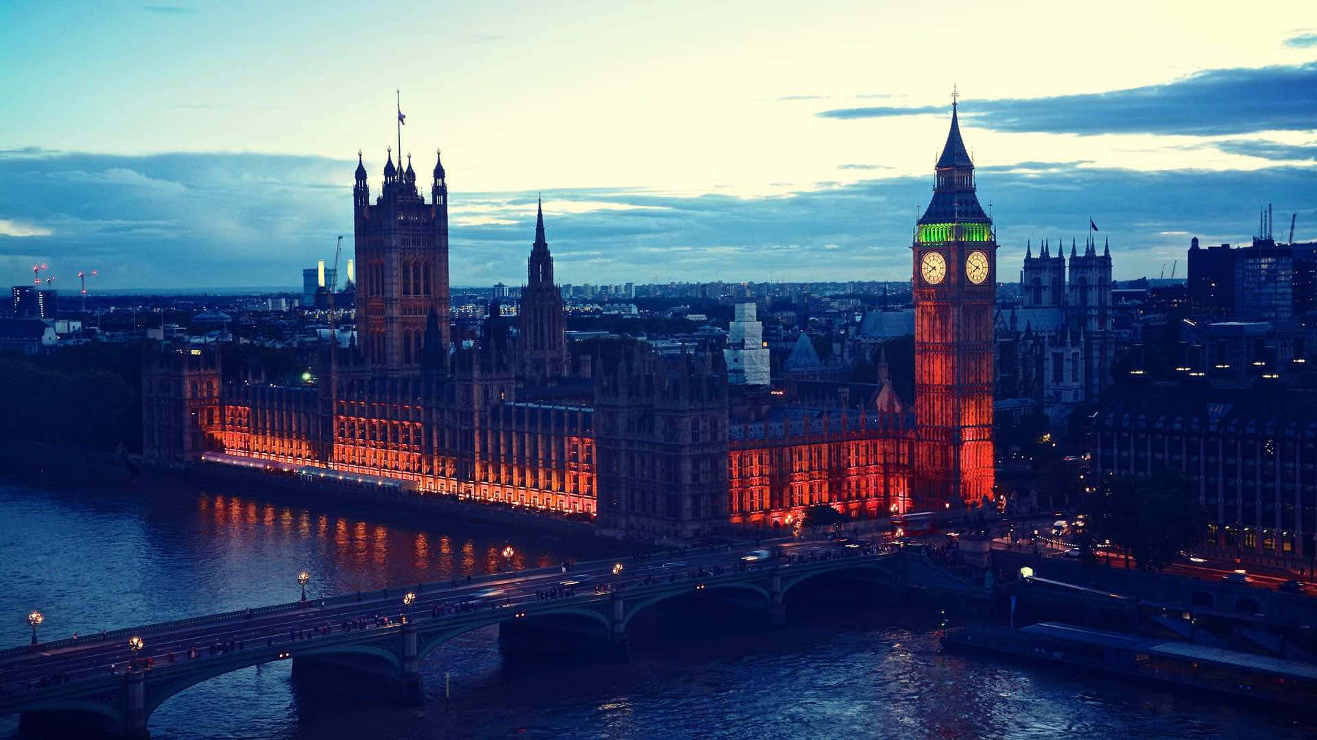 England 桌布 壁紙 — 倫敦標誌性的大笨鐘和國會大廈在暮色藍天下溫暖地發光，泰晤士河倒映著它們的燈光。
