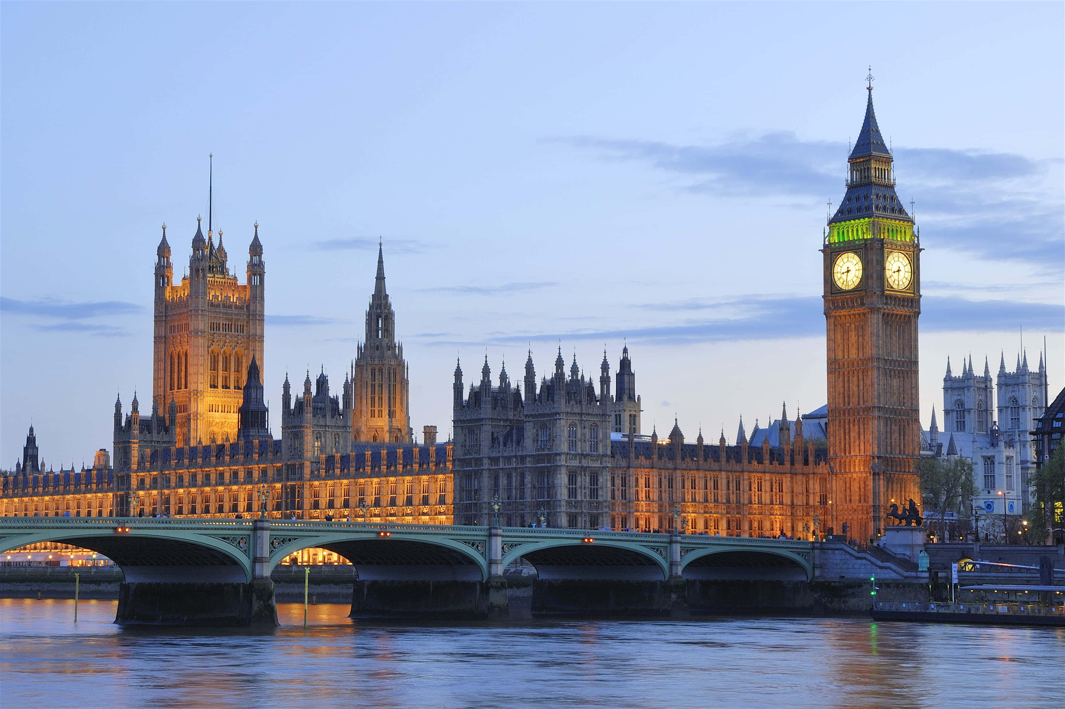 England 桌布 壁紙 — 倫敦標誌性的大笨鐘和國會大廈在黃昏時亮燈，倒映在泰晤士河上，前景有一座橋。