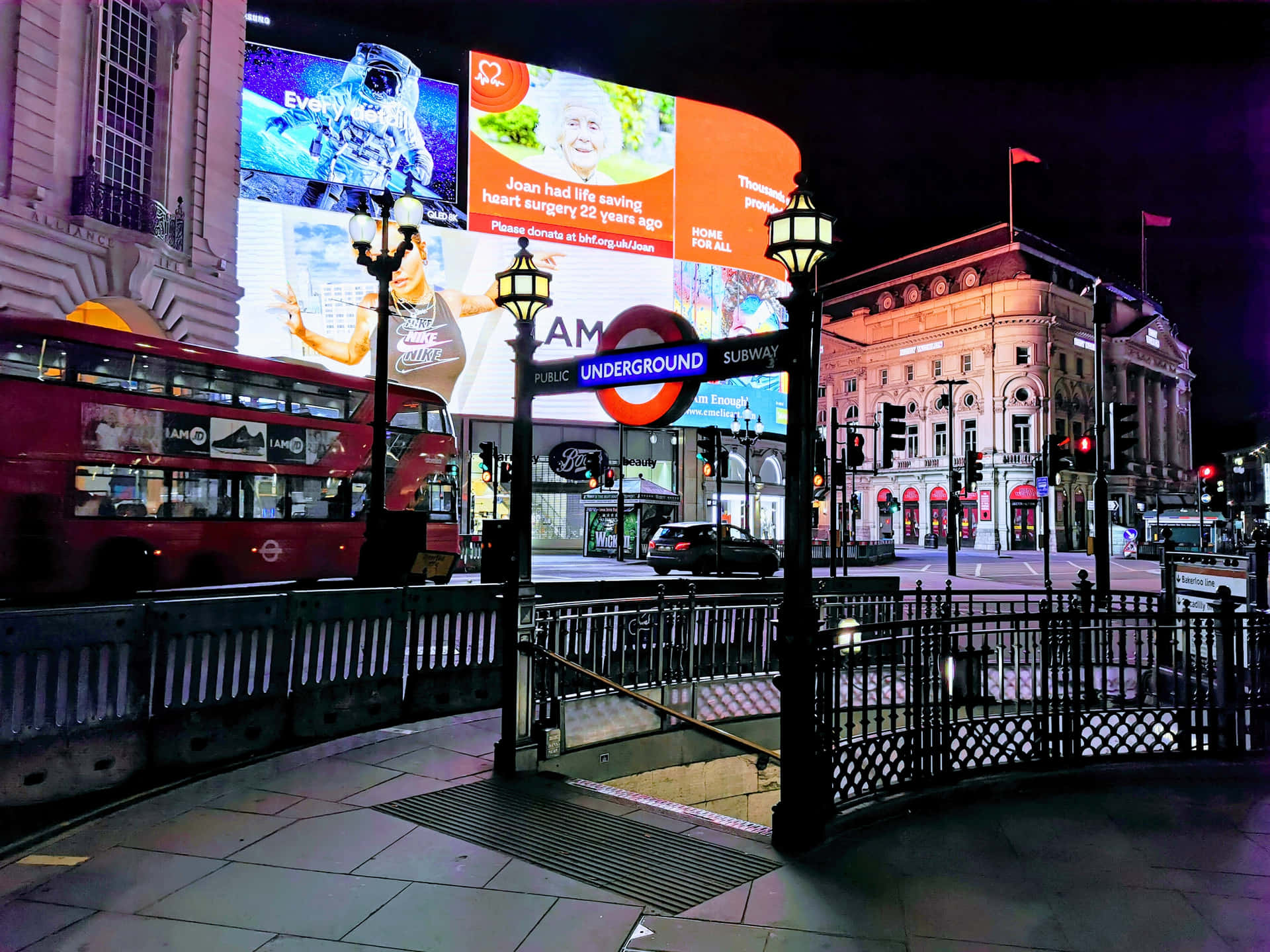 倫敦皮卡迪利圓環夜景城市燈光 壁紙 — 倫敦充滿活力的夜景，一輛紅色雙層巴士駛過發光的地鐵入口，巨大的數碼廣告牌照亮了歷史建築。