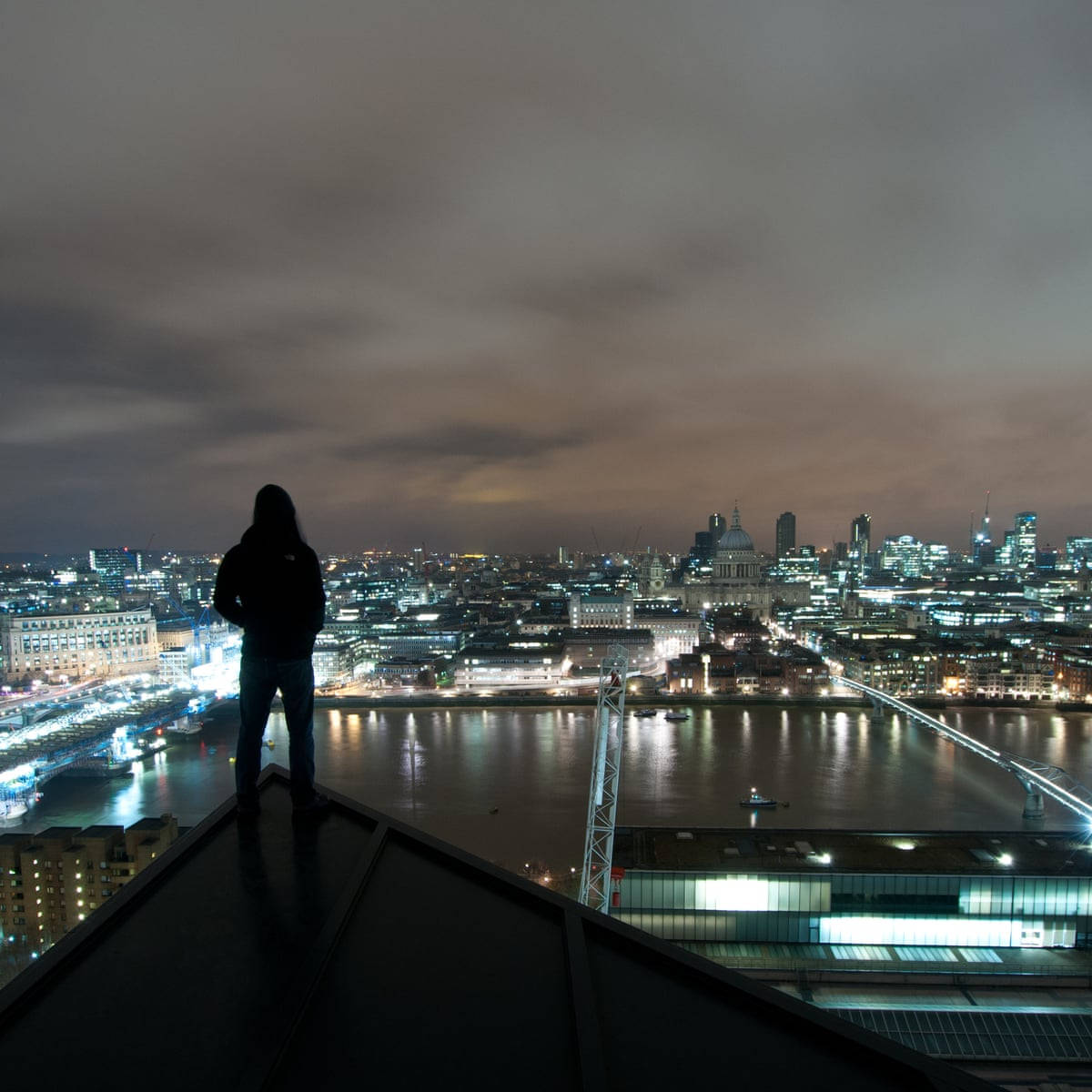 倫敦都市夜景 壁紙 — 一個孤獨的身影站在屋頂上，俯瞰夜晚倫敦閃爍的天際線，泰晤士河倒映著城市的燈光。