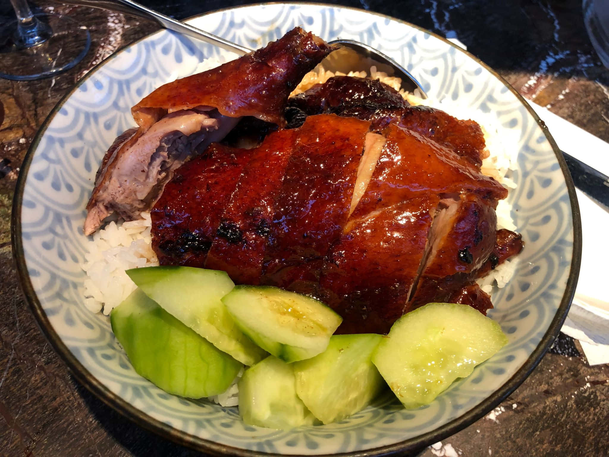 倫敦鴨與米餐廳的鴨飯 壁紙 — 一隻油亮嘅脆皮燒鴨放喺白飯上面，旁邊有新鮮青瓜片，用一個有圖案嘅碗盛載。