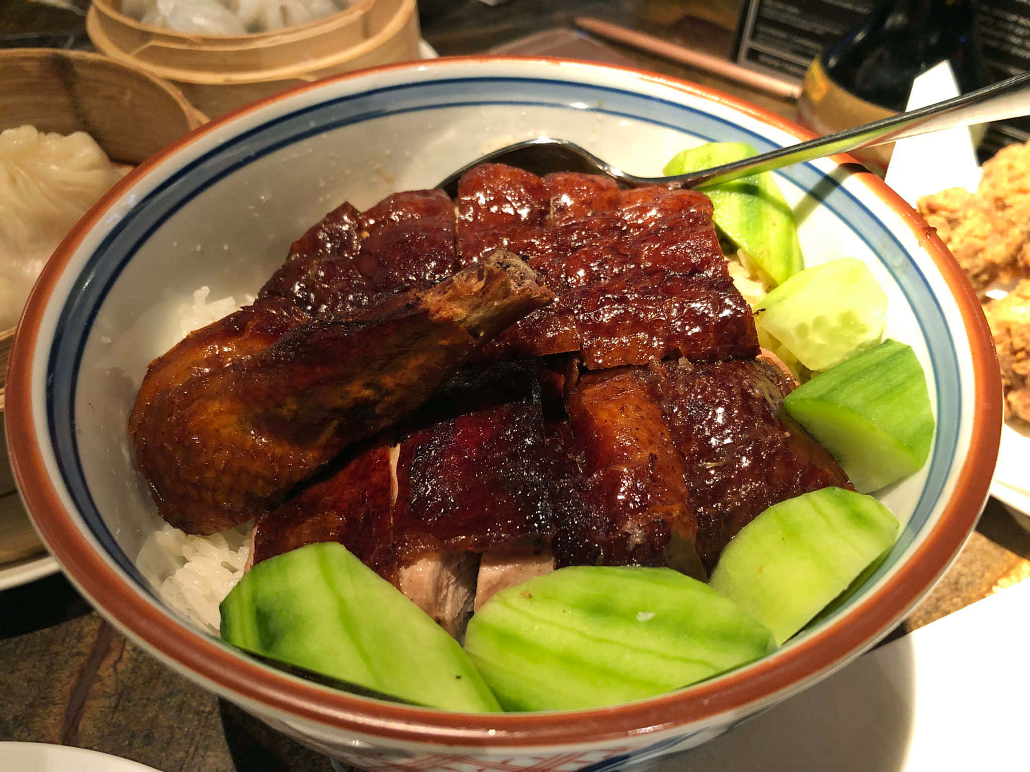 倫敦鴨與米餐廳的鴨飯 壁紙 — 一個光澤烤鴨碗的特寫，碗內有米飯和切片青瓜，放在陶瓷碗中。