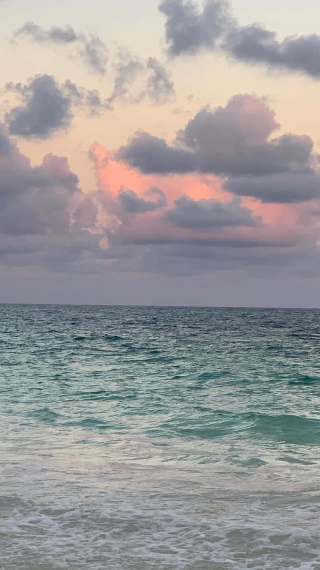 日落時分的海浪，天空中有粉紅色和灰色的雲彩。