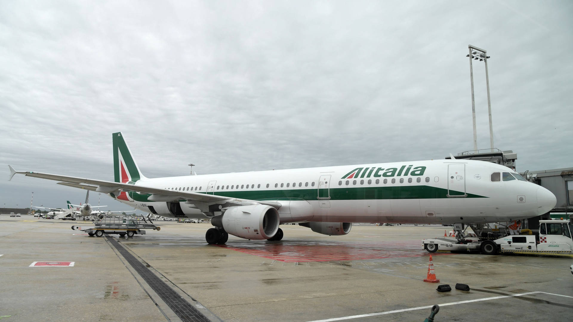 意大利航空飛機停在機場閘口，濕滑停機坪上有地勤人員和設備。