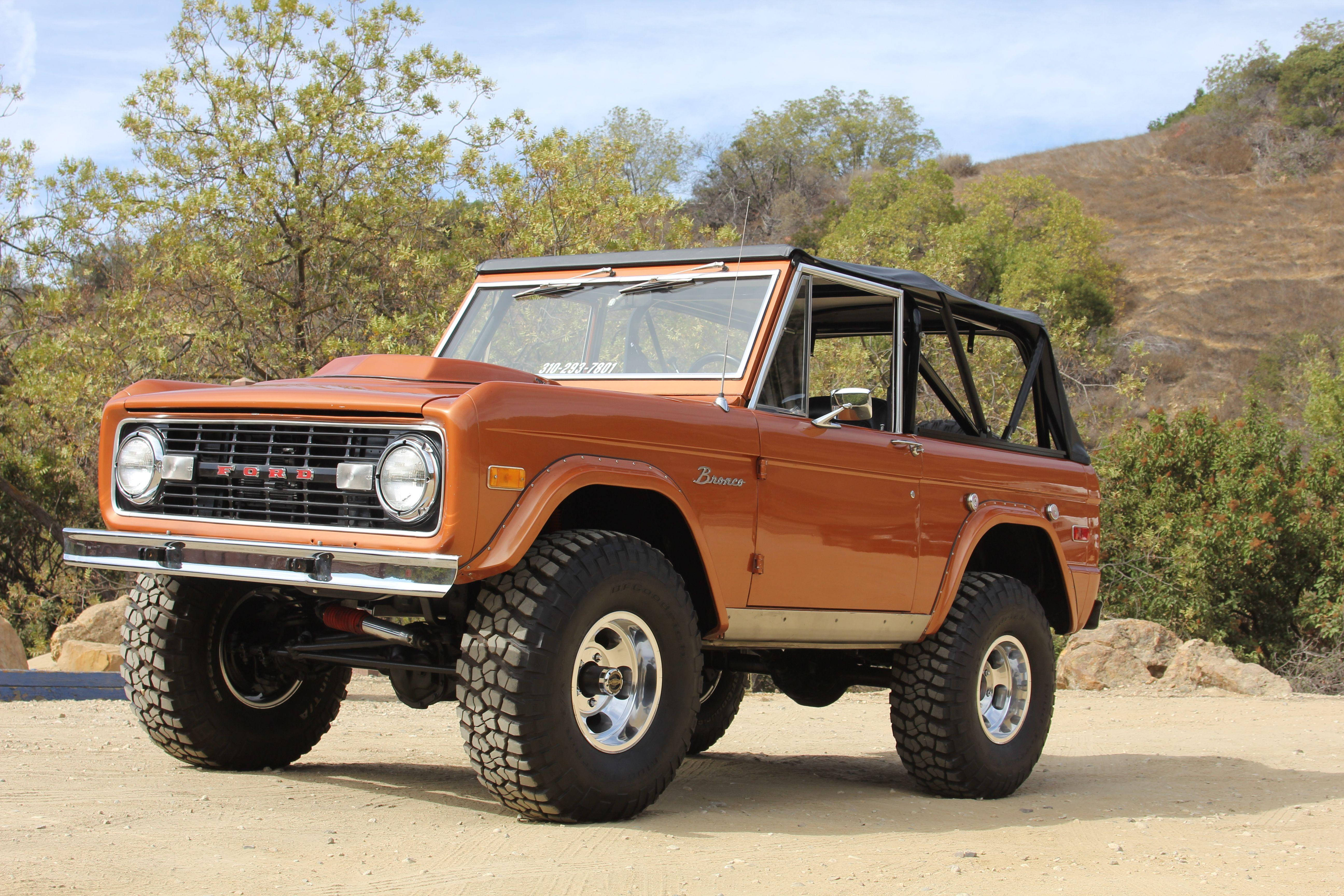 停泊於土路的福特 Bronco 壁紙 — 一輛復古橙色福特Bronco，帶黑色防滾架，停在塵土飛揚的地形上，天空清澈湛藍。